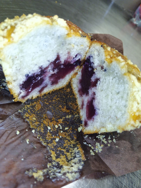 Muffin ripieno di mirtilli tagliato, che rivela un ripieno di frutti di bosco scuri, una copertura friabile e leggera e una fodera di carta marrone.