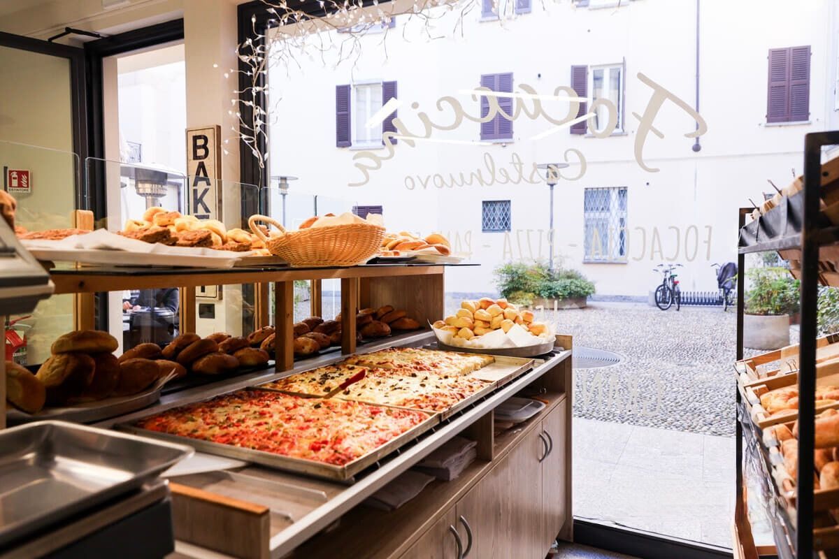 Un'esposizione di prodotti da forno con vari prodotti da forno, tra cui pizza, pasticcini e pane, visibili attraverso una vetrina.