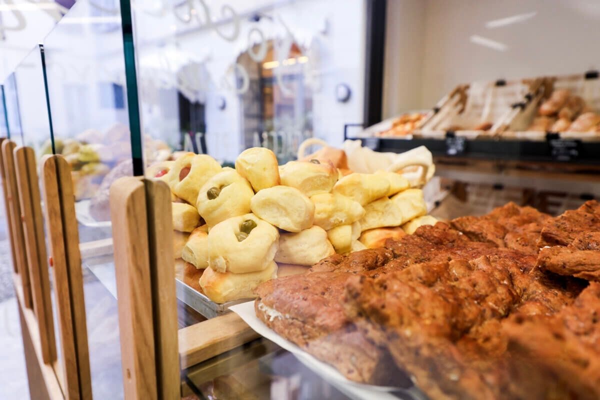 Fornaio in una panetteria con pasticceria, indossa berretto e guanti e prepara un panino.