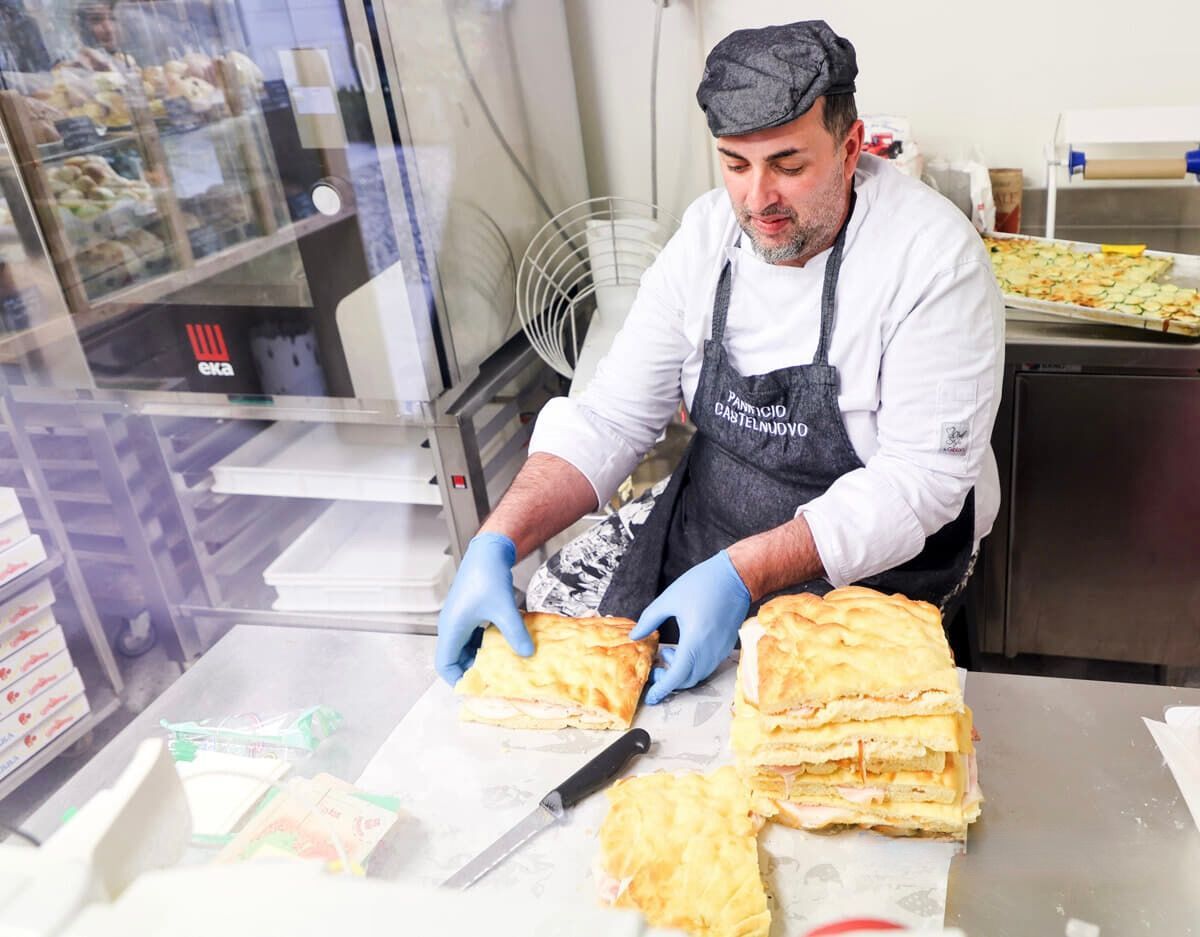 Fornaio in una panetteria con pasticceria, indossa berretto e guanti e prepara un panino.