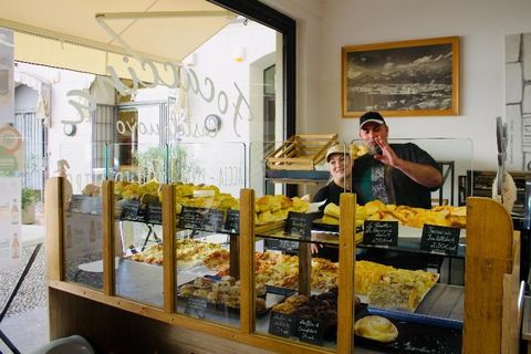 Bancone del panificio con prodotti da forno e due persone sorridenti, una delle quali fa un gesto di pollice in su.