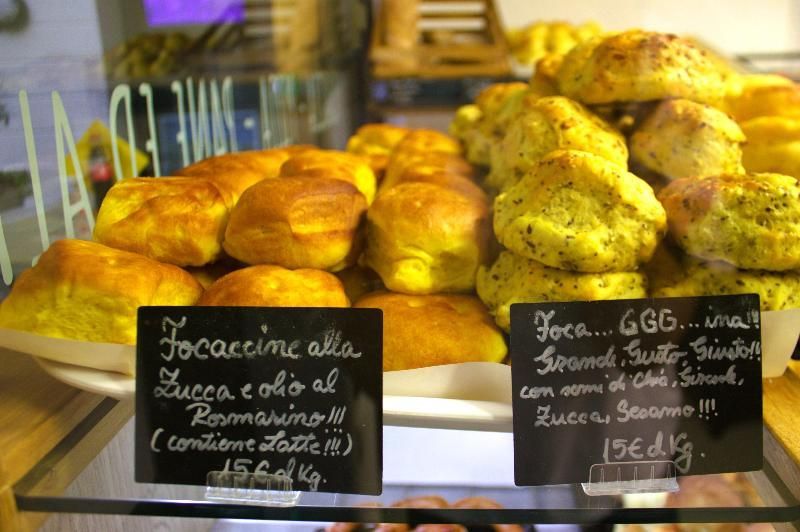 Prodotti da forno, focaccine, con cartelli che elencano ingredienti e prezzi.