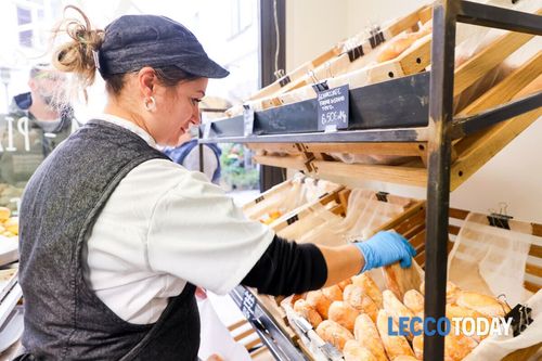 Un fornaio sistema il pane sugli scaffali. Indossa berretto, grembiule e guanti all'interno di un panificio.