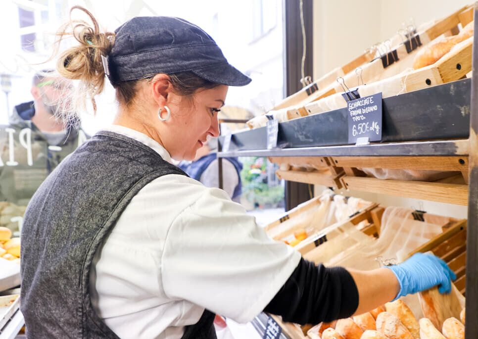 Bancone del panificio con prodotti da forno e due persone sorridenti, una delle quali fa un gesto di pollice in su.