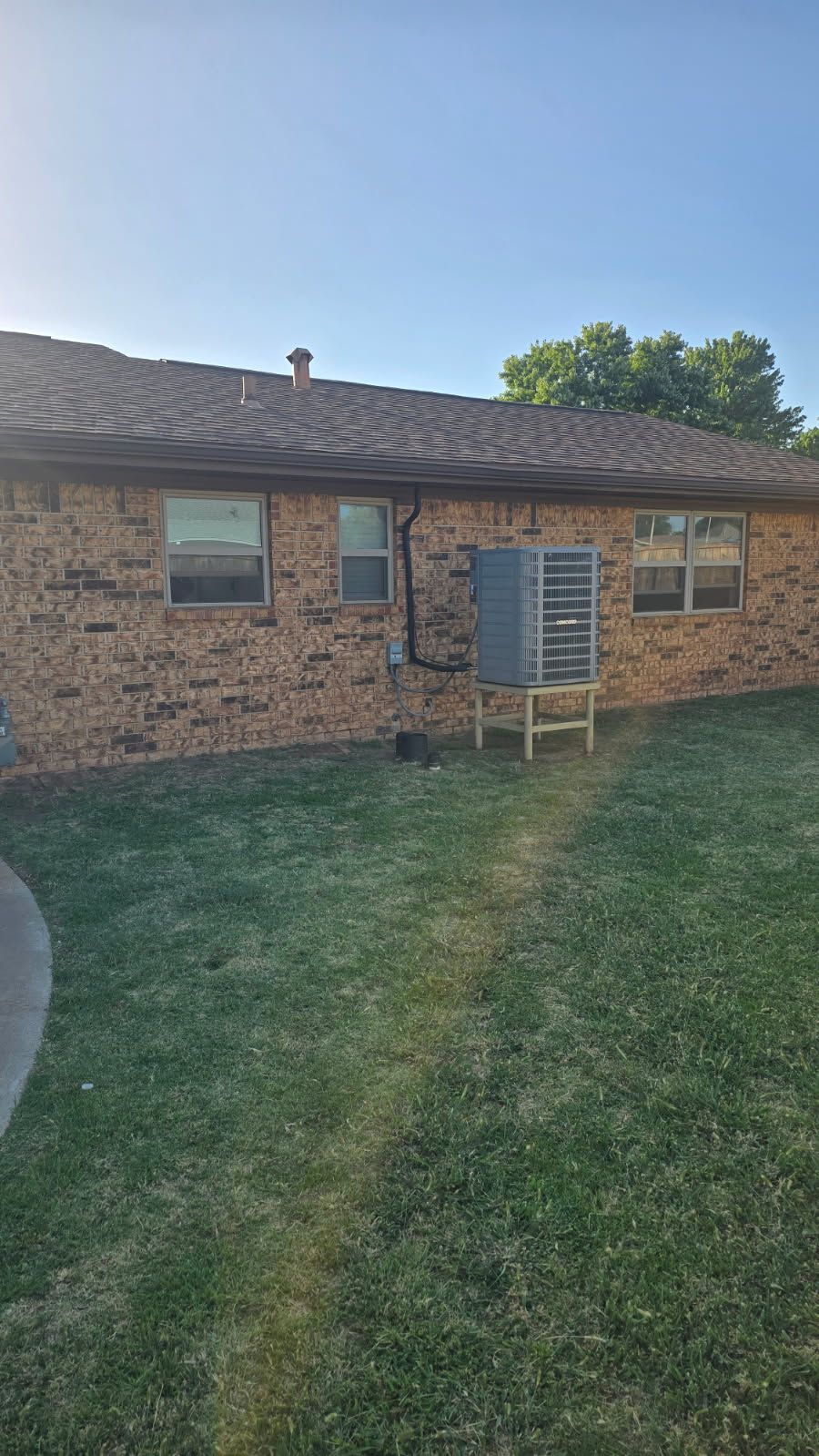 Brick house exterior with two windows, a metal air conditioning unit, and green lawn under a clear blue sky.