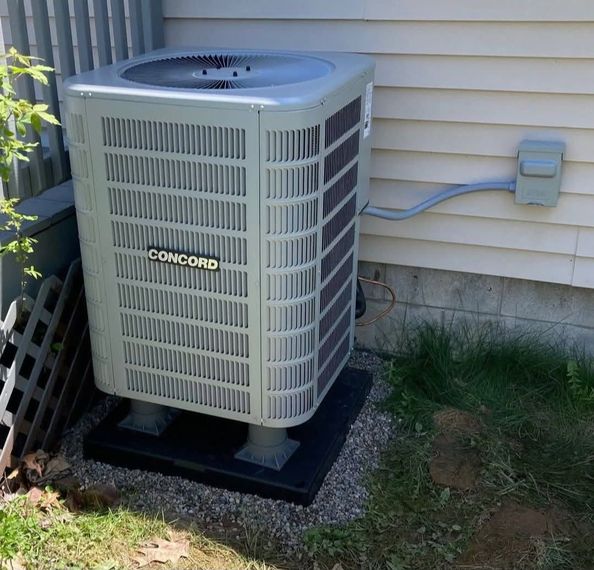 Concord air conditioning unit outside a white house. The unit is gray, and sits on a black base in the grass.