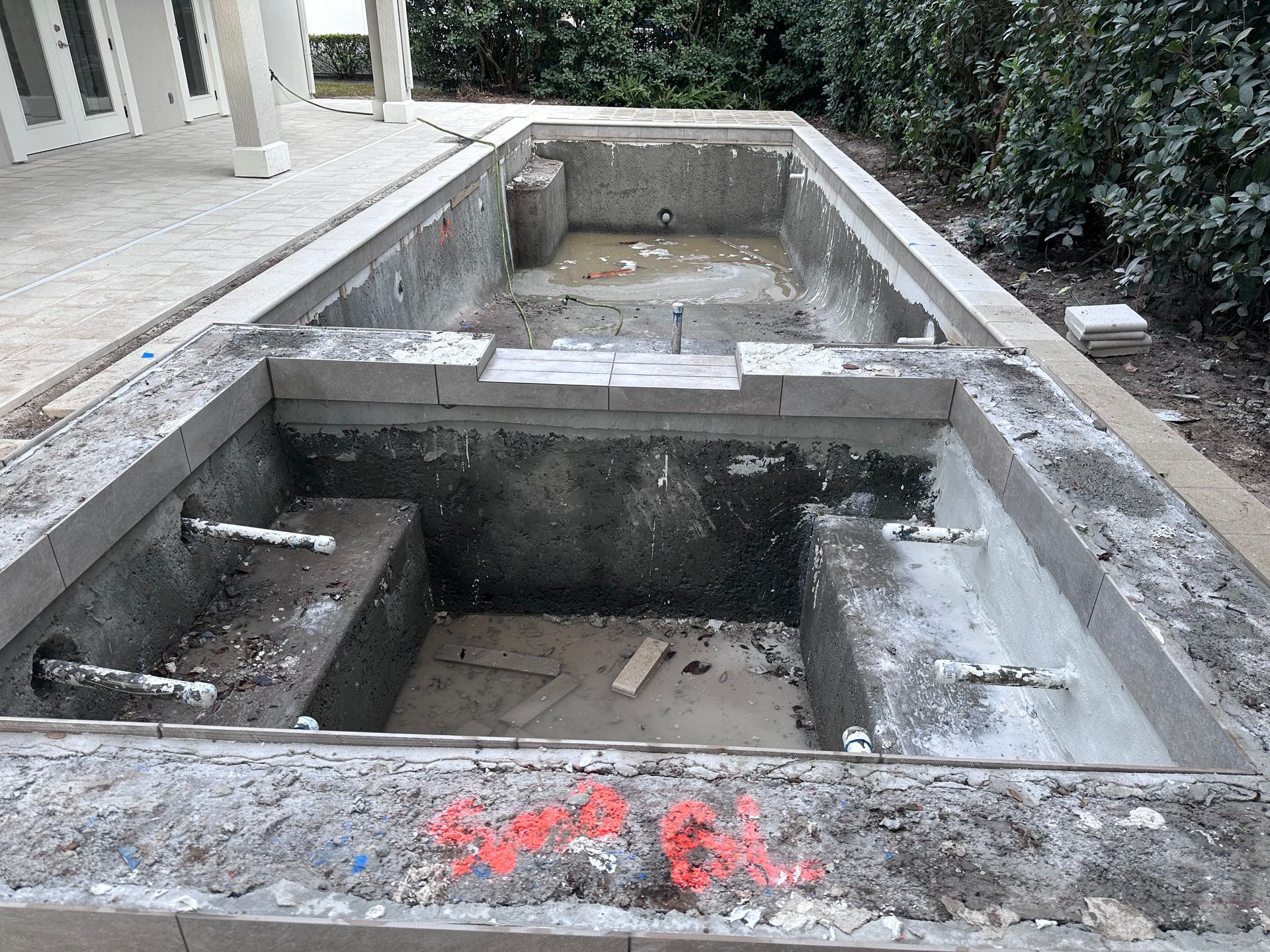 Empty concrete pool under construction; includes two sunken sections and patio access.