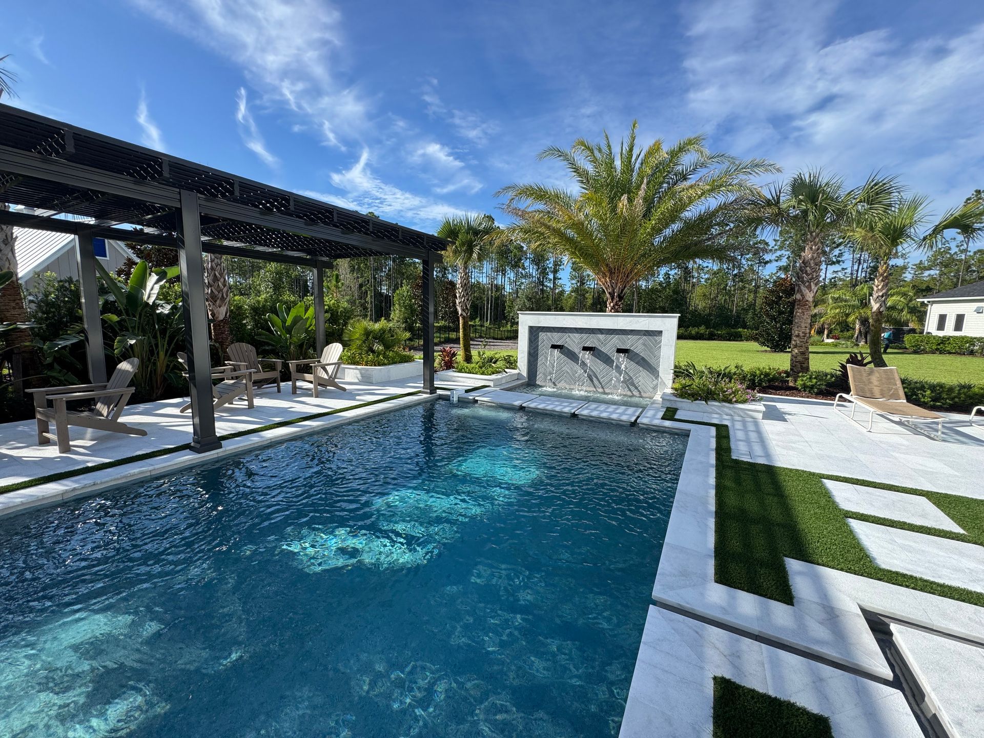 Pool with pergola, dolphin fountain, palm trees, blue water, and white patio.