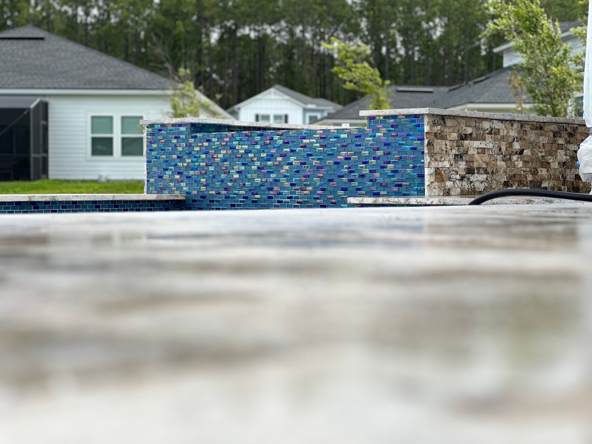 Poolside mosaic wall with houses in background.