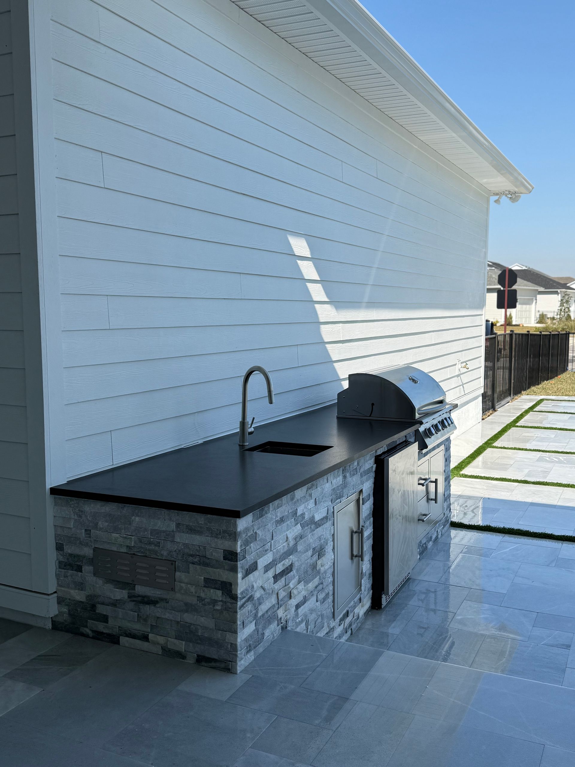Outdoor kitchen with grill, sink, and stone facade against a white wall.