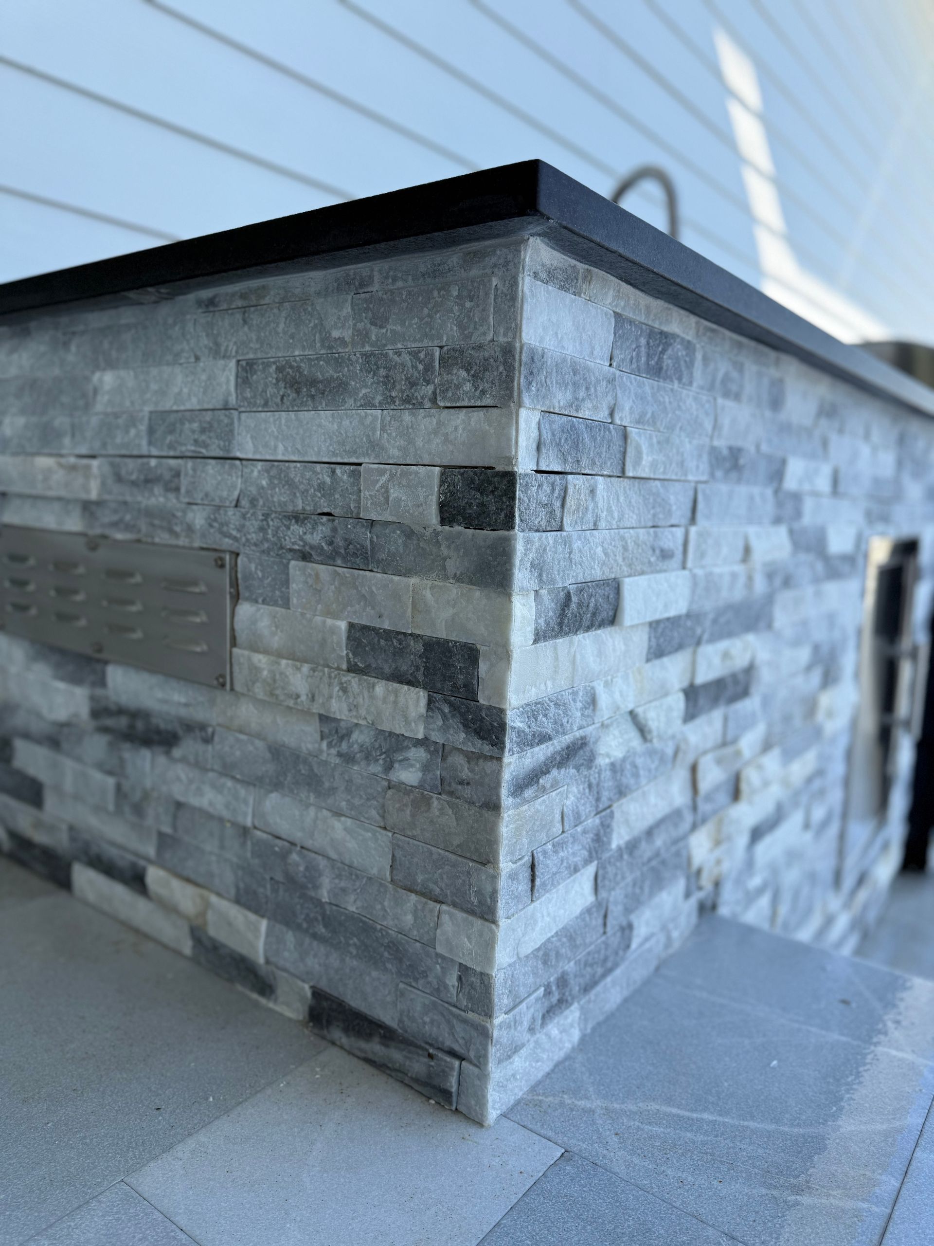 Gray stone outdoor kitchen corner with black countertop.