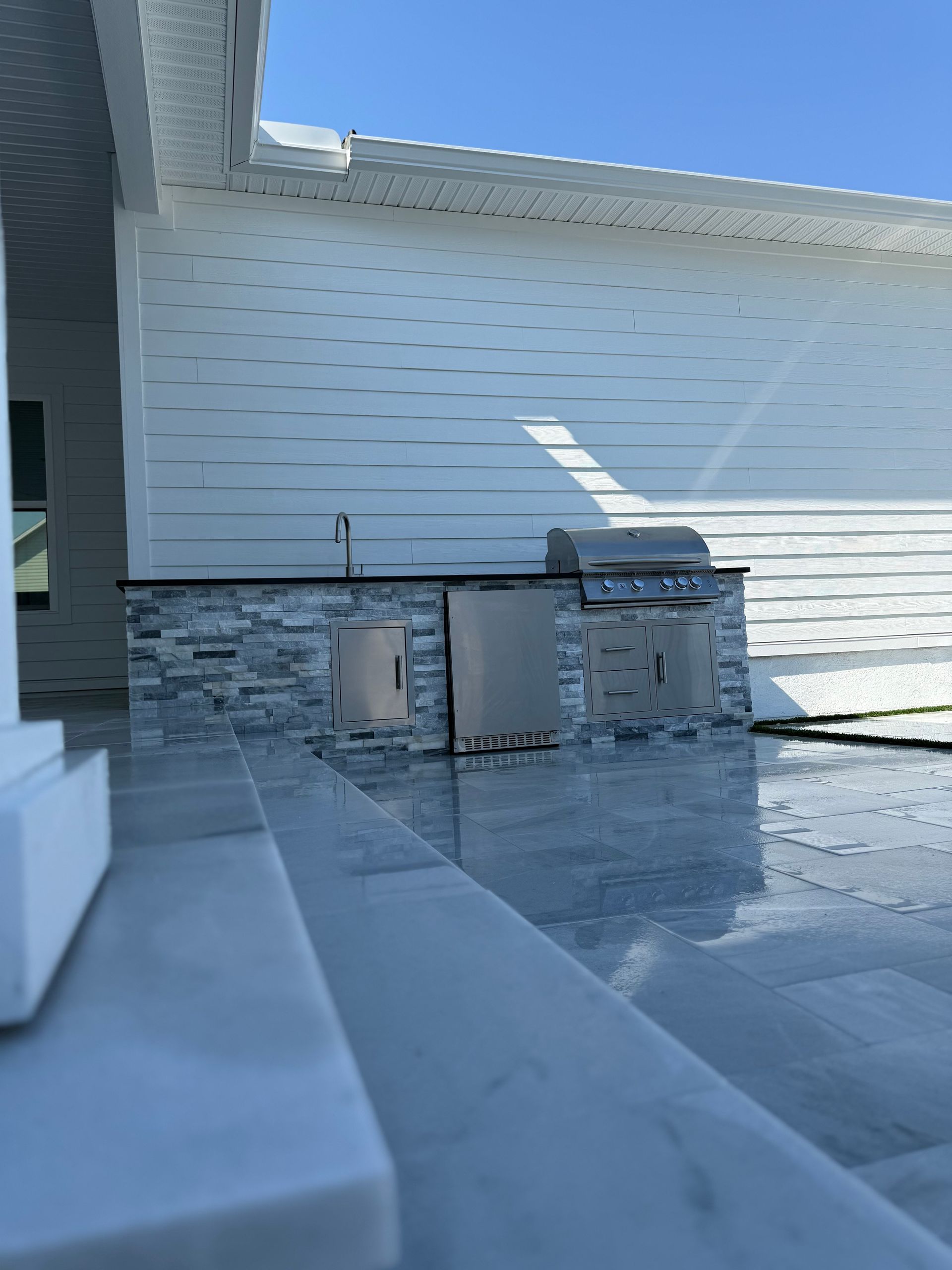 Outdoor kitchen with gray stone base, stainless steel grill and cabinets.