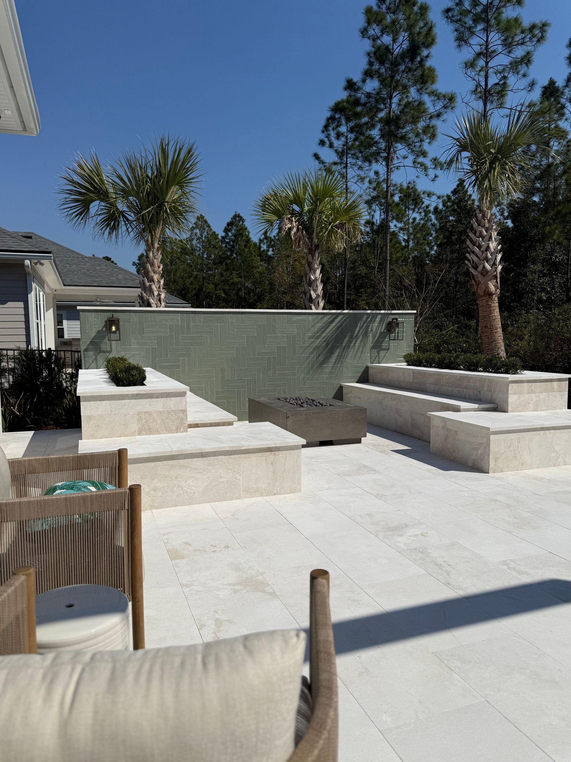 Outdoor patio with tiered seating, a water feature, and palm trees under a blue sky.