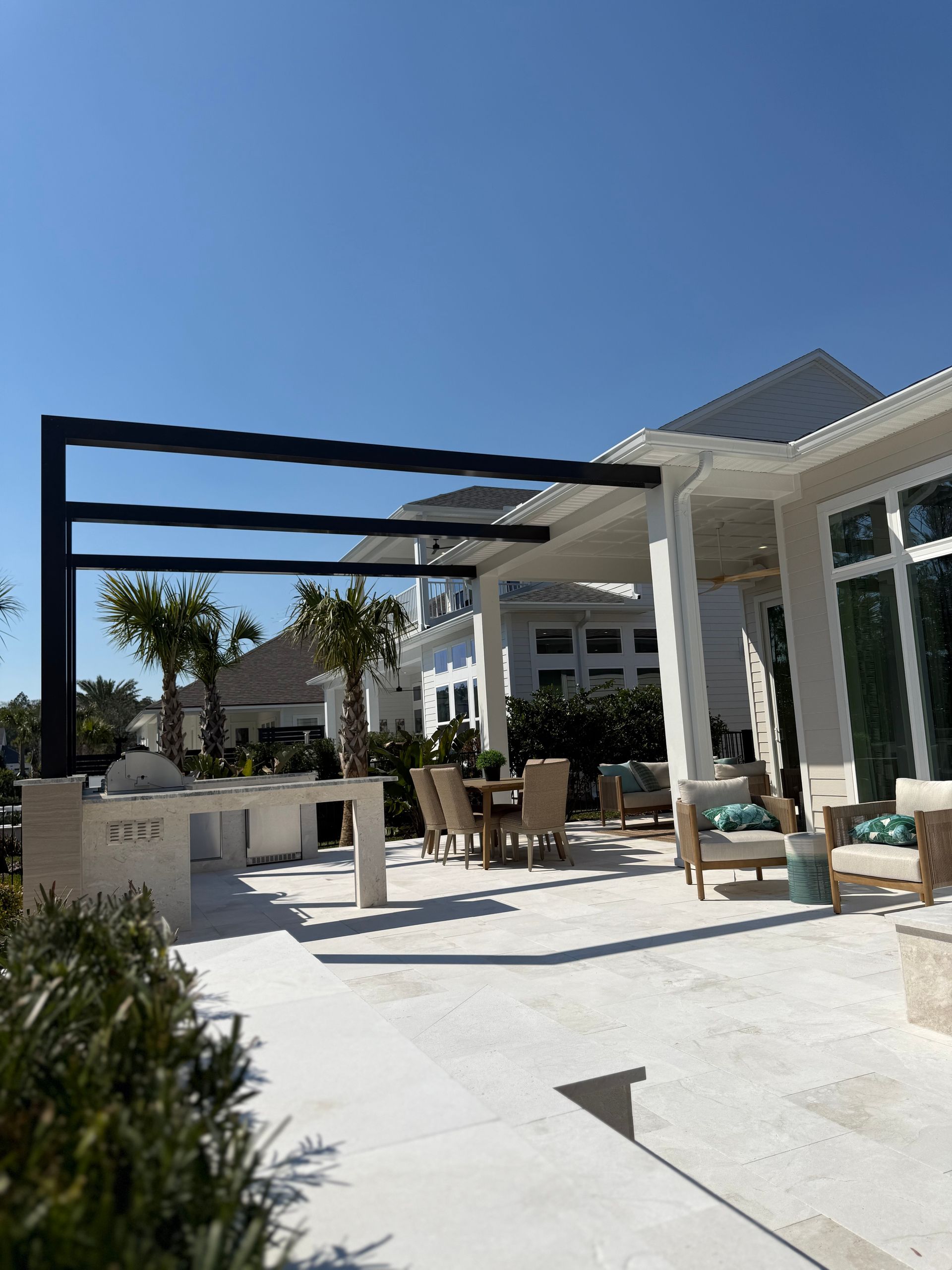 Outdoor patio with a black pergola, kitchen, and seating area on a sunny day.