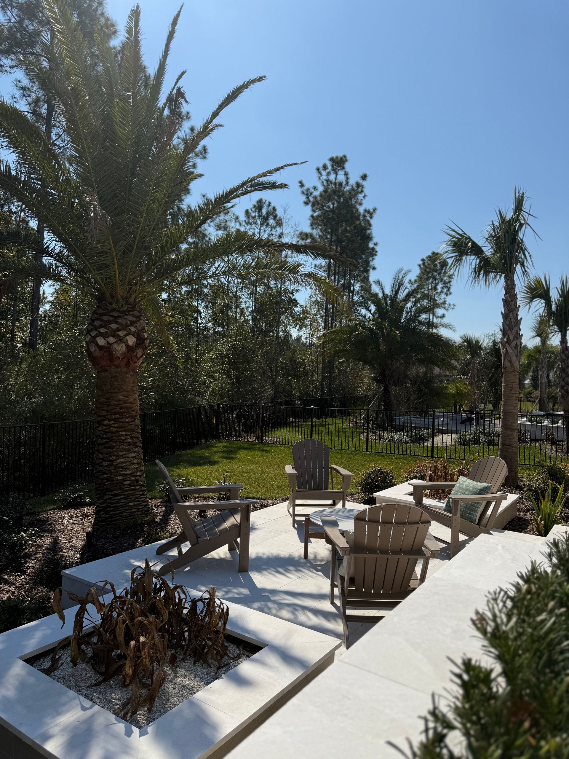 Outdoor seating area with wooden chairs on a stone patio surrounded by greenery and palm trees.