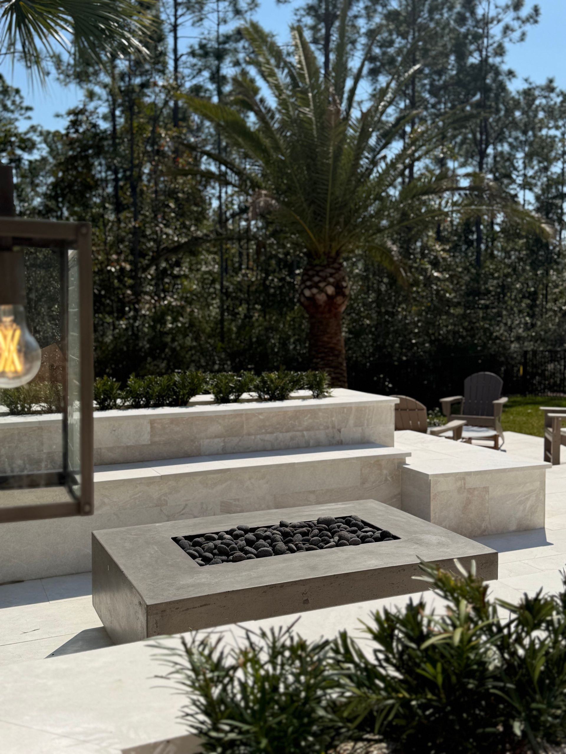 Outdoor patio with a concrete fire pit, tiered planters, and a palm tree.