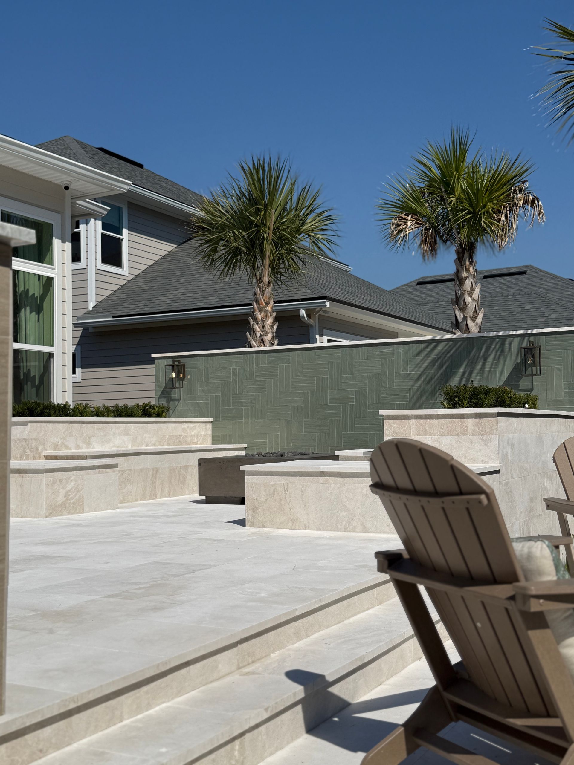 Outdoor patio with palm trees, steps, seating, and a turquoise wall, in bright sunlight.