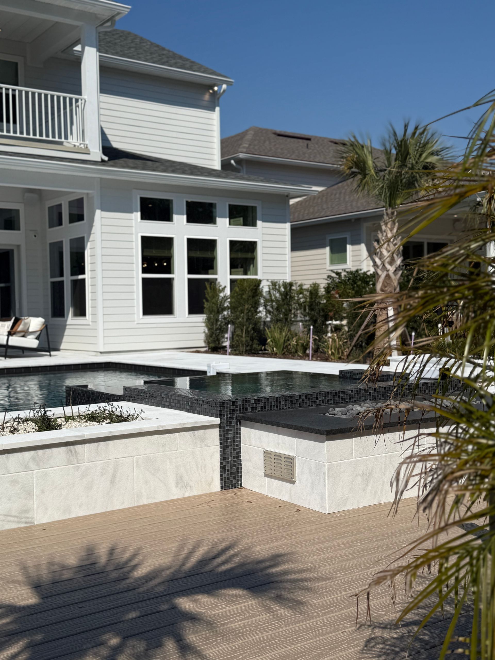 Swimming pool with a white tile deck and a light-colored house in the background.