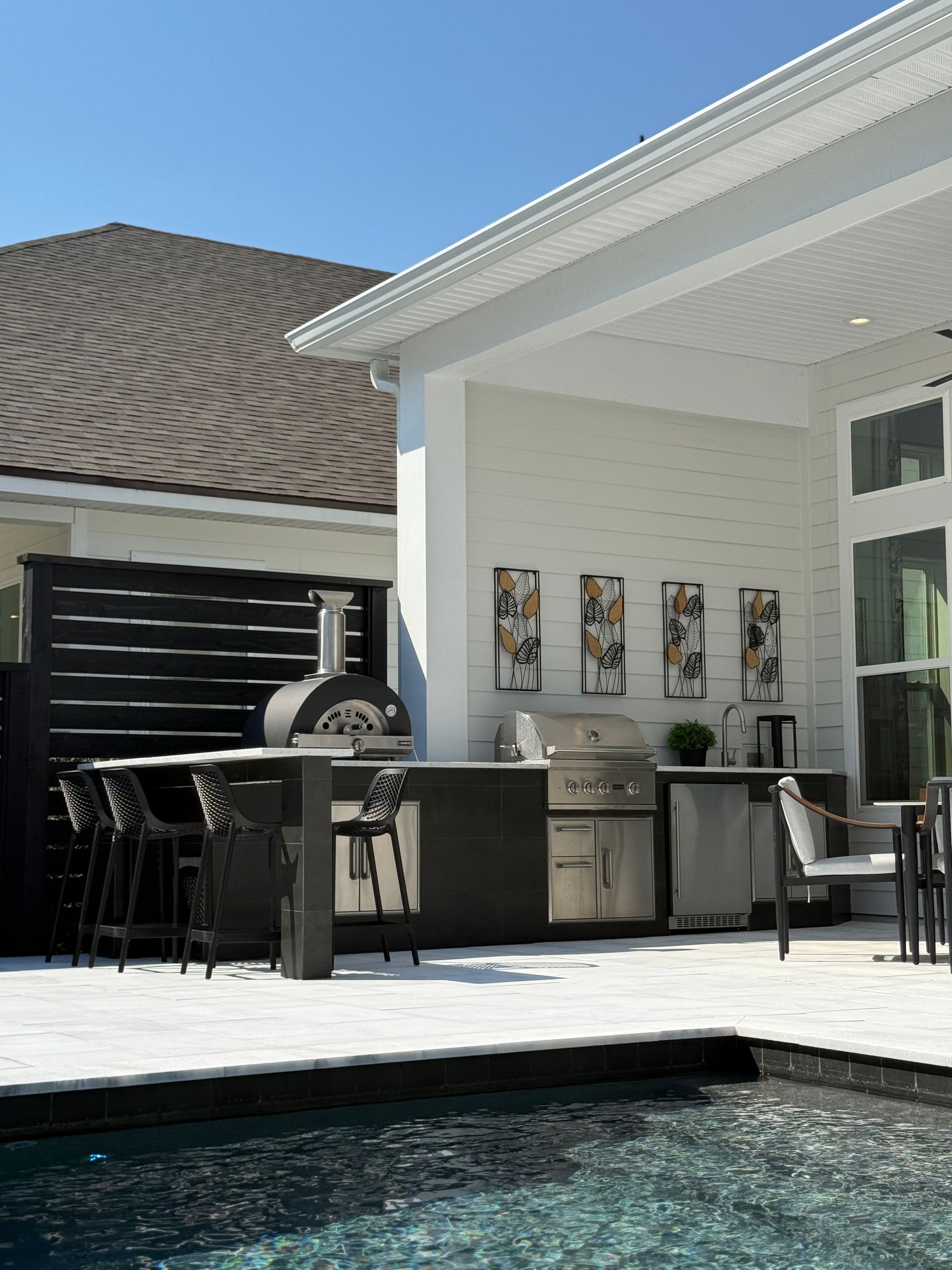 Outdoor kitchen with a pizza oven, grill, and bar overlooking a pool.