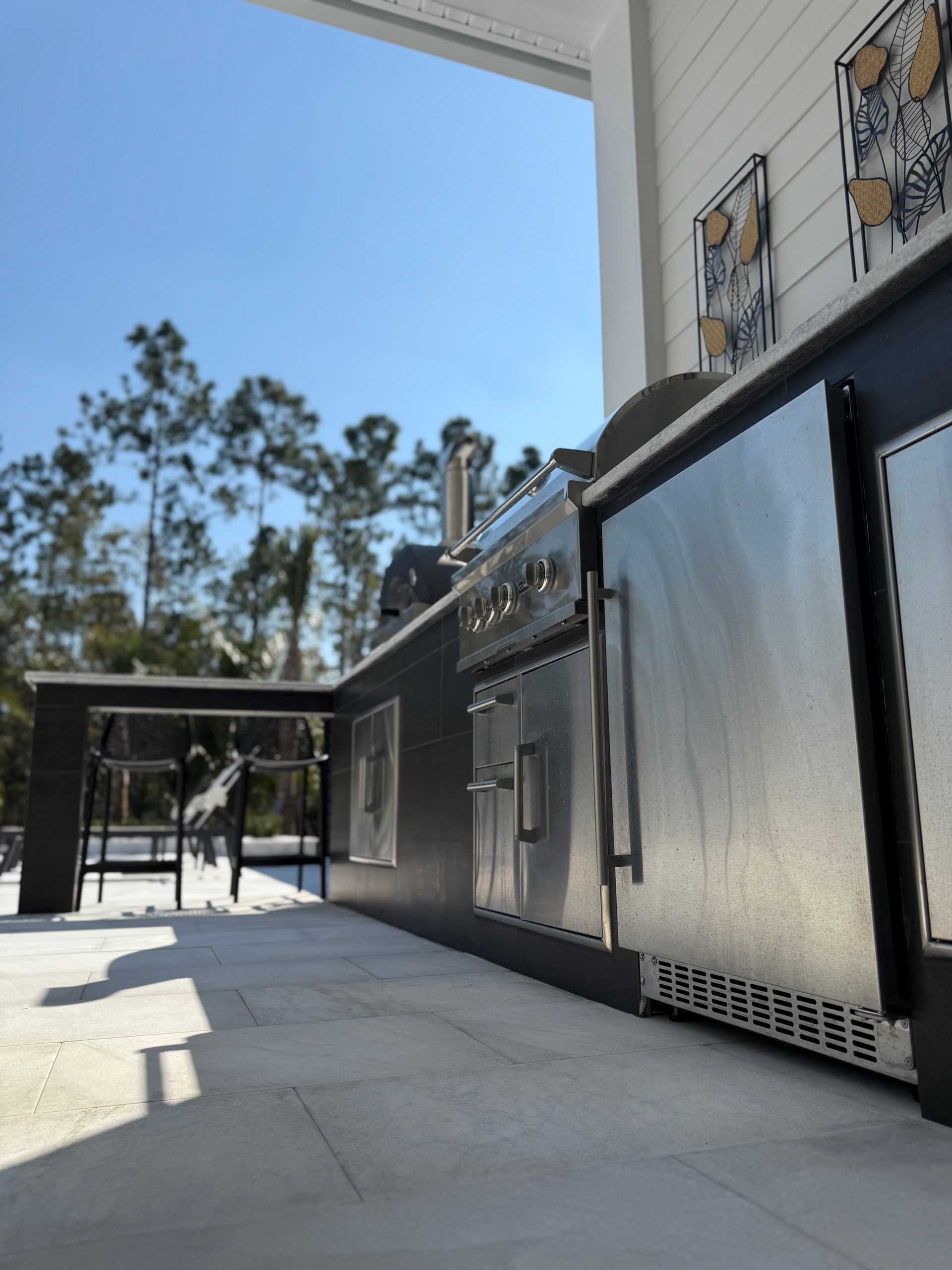 Outdoor kitchen with stainless steel appliances and black cabinets on a stone patio.