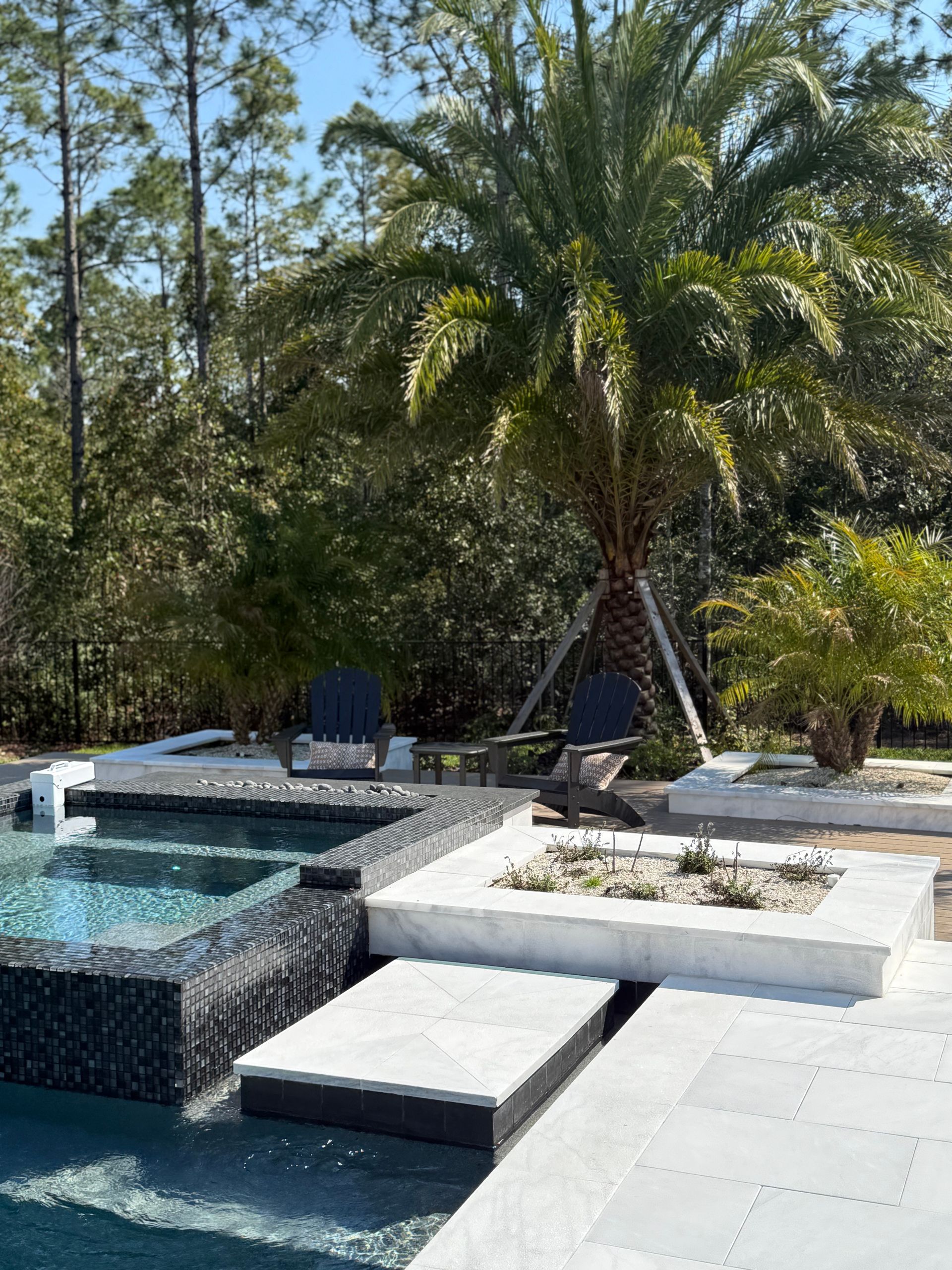 Poolside scene with a palm tree, pool, seating area, and lush greenery.