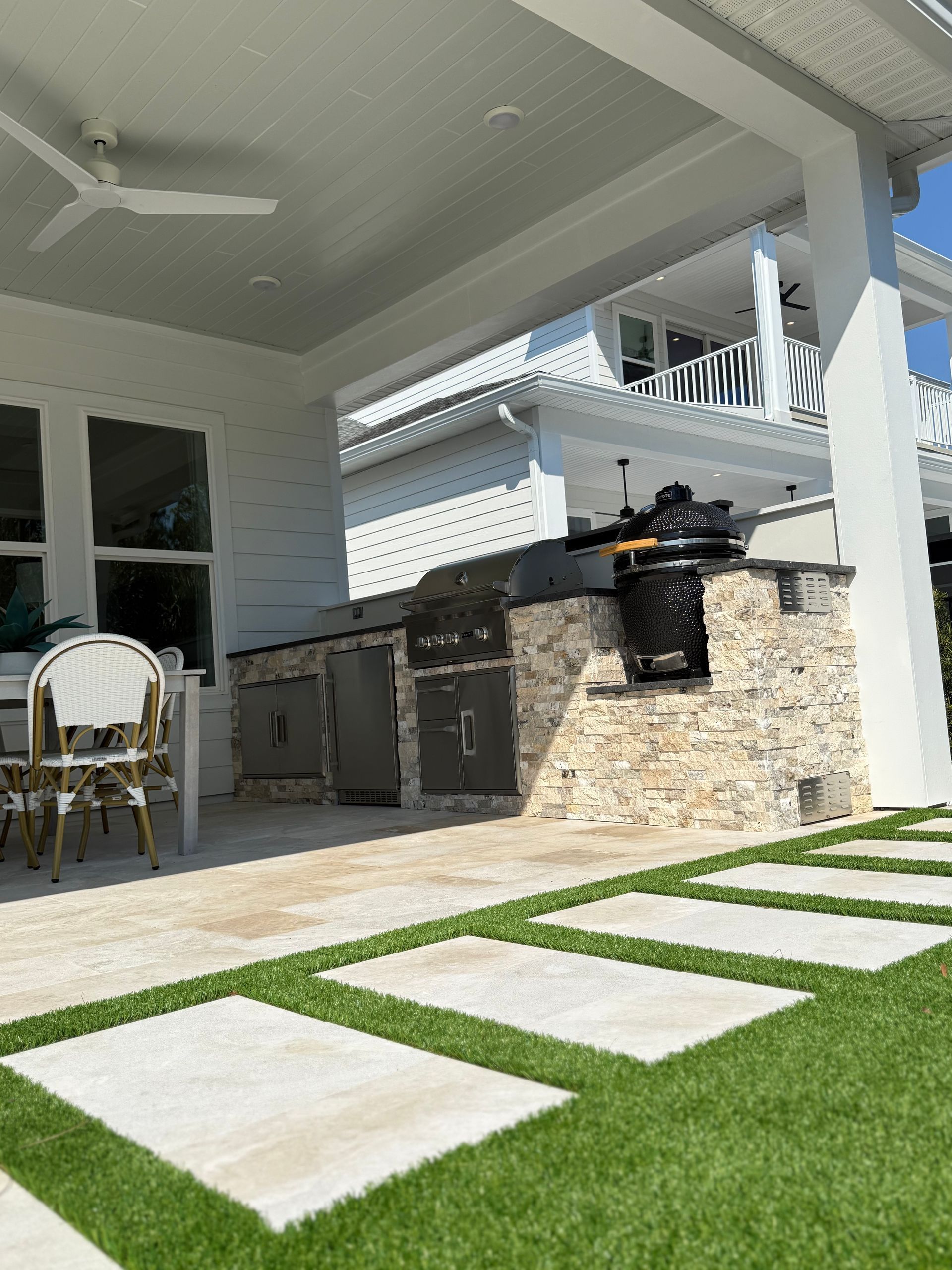 Outdoor kitchen with a grill, in a white house with blue sky.