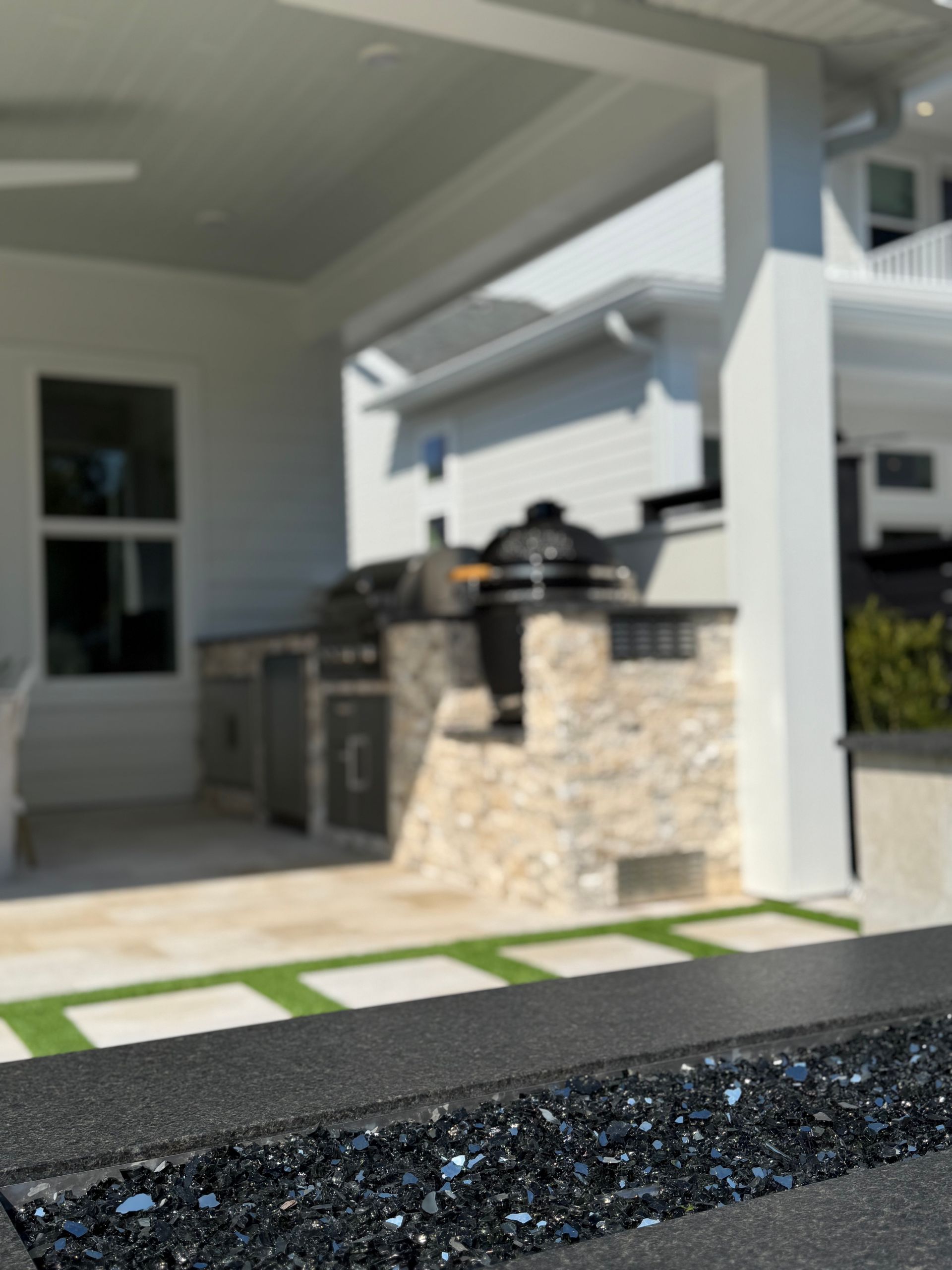 Outdoor kitchen with grill, bar, white columns, and black countertop, set against a bright building.