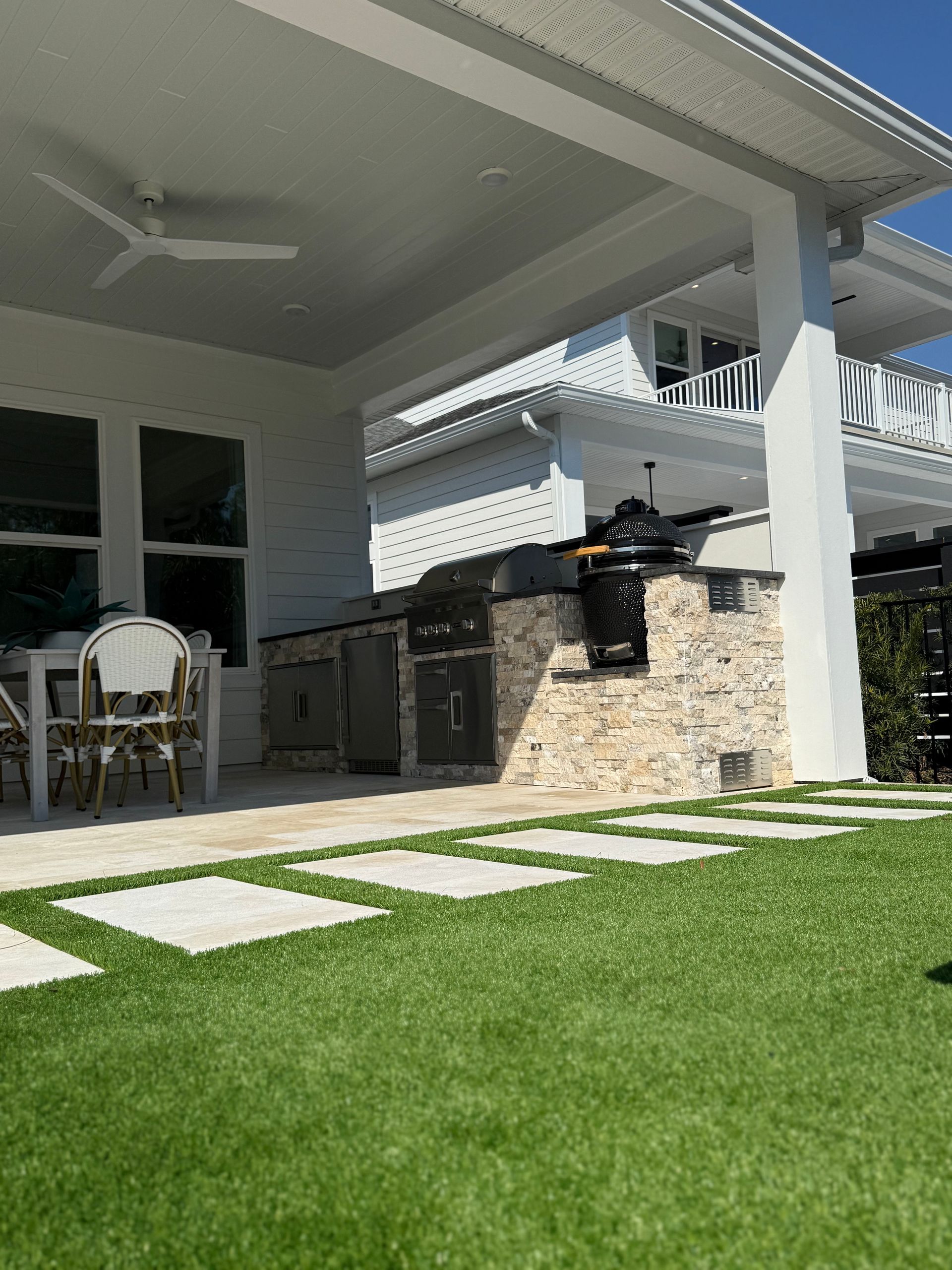 Outdoor kitchen with a grill, stone facade, and patio with grass and stepping stones.