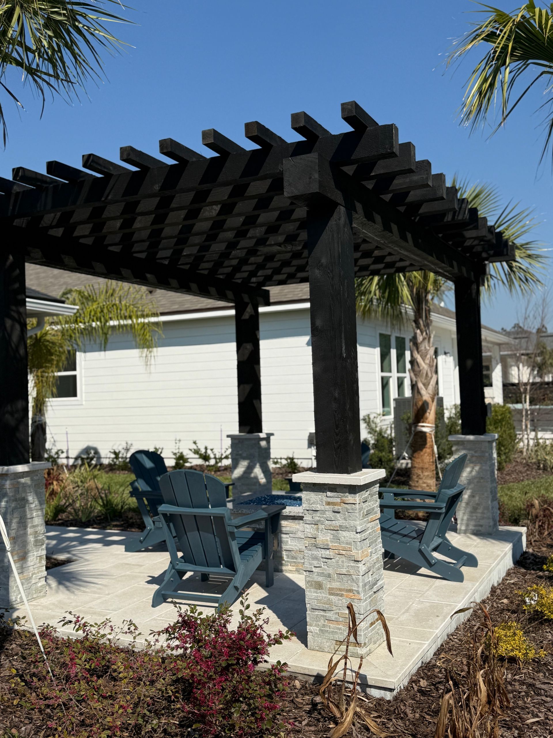 Pergola with blue Adirondack chairs on concrete patio.
