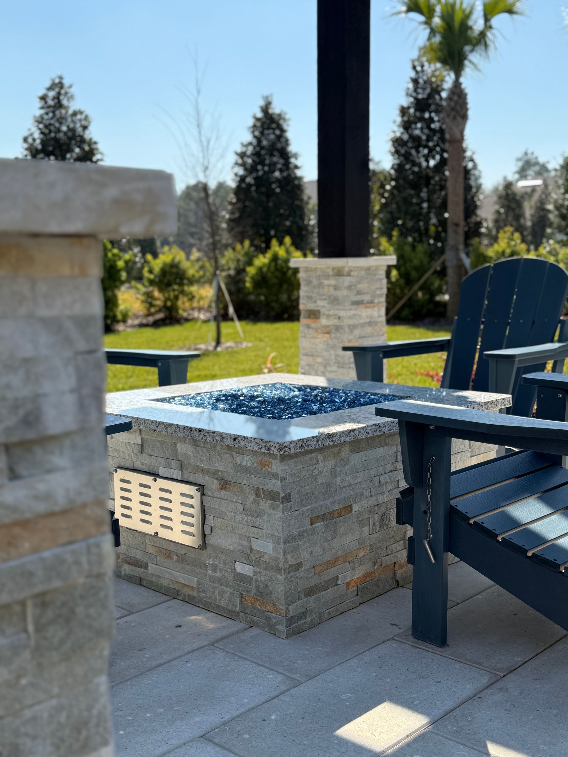 Outdoor fire pit with blue fire glass, stone surround, and blue Adirondack chairs.
