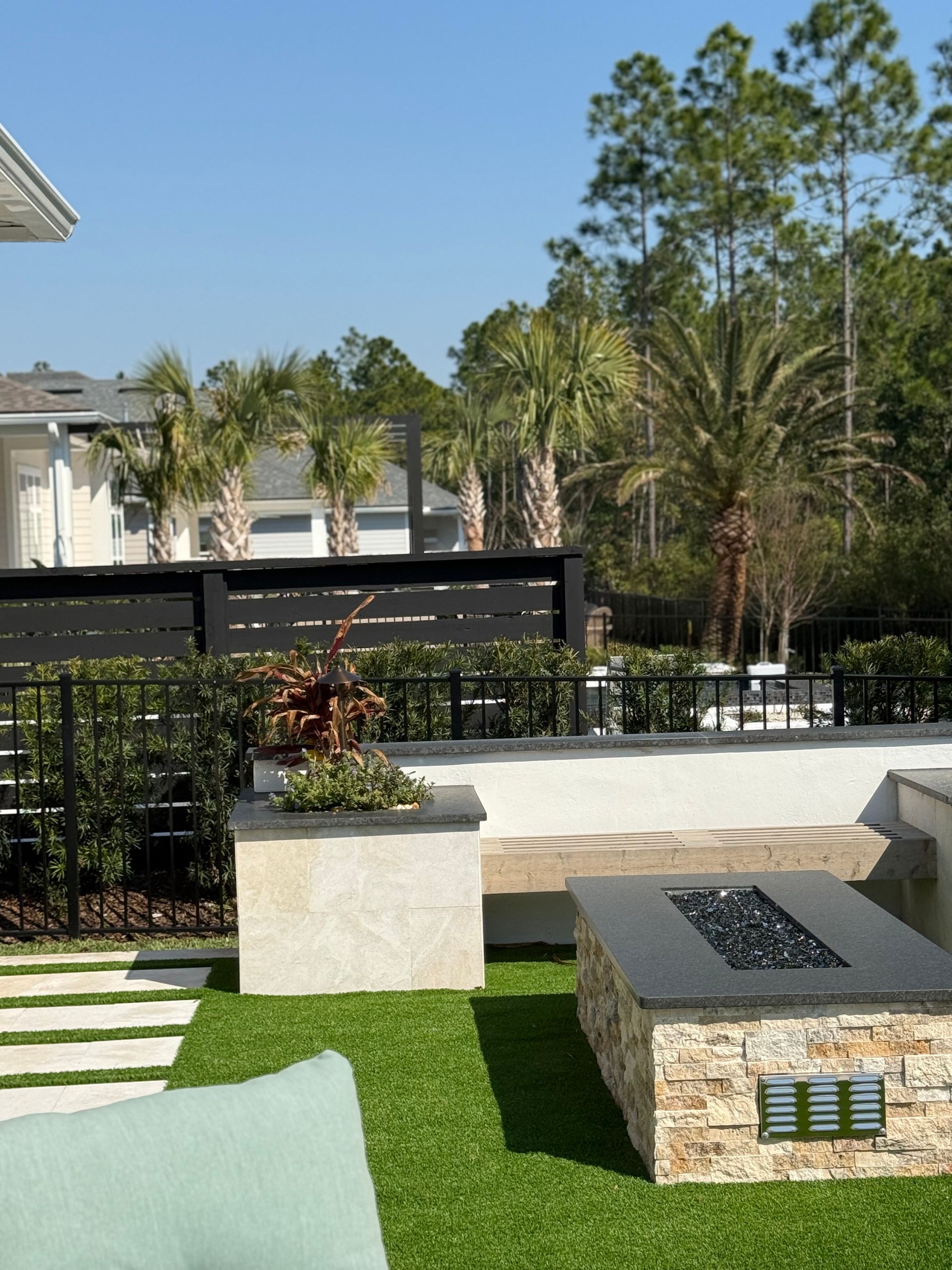Backyard patio with artificial turf, fire pit, planters, and black fence.