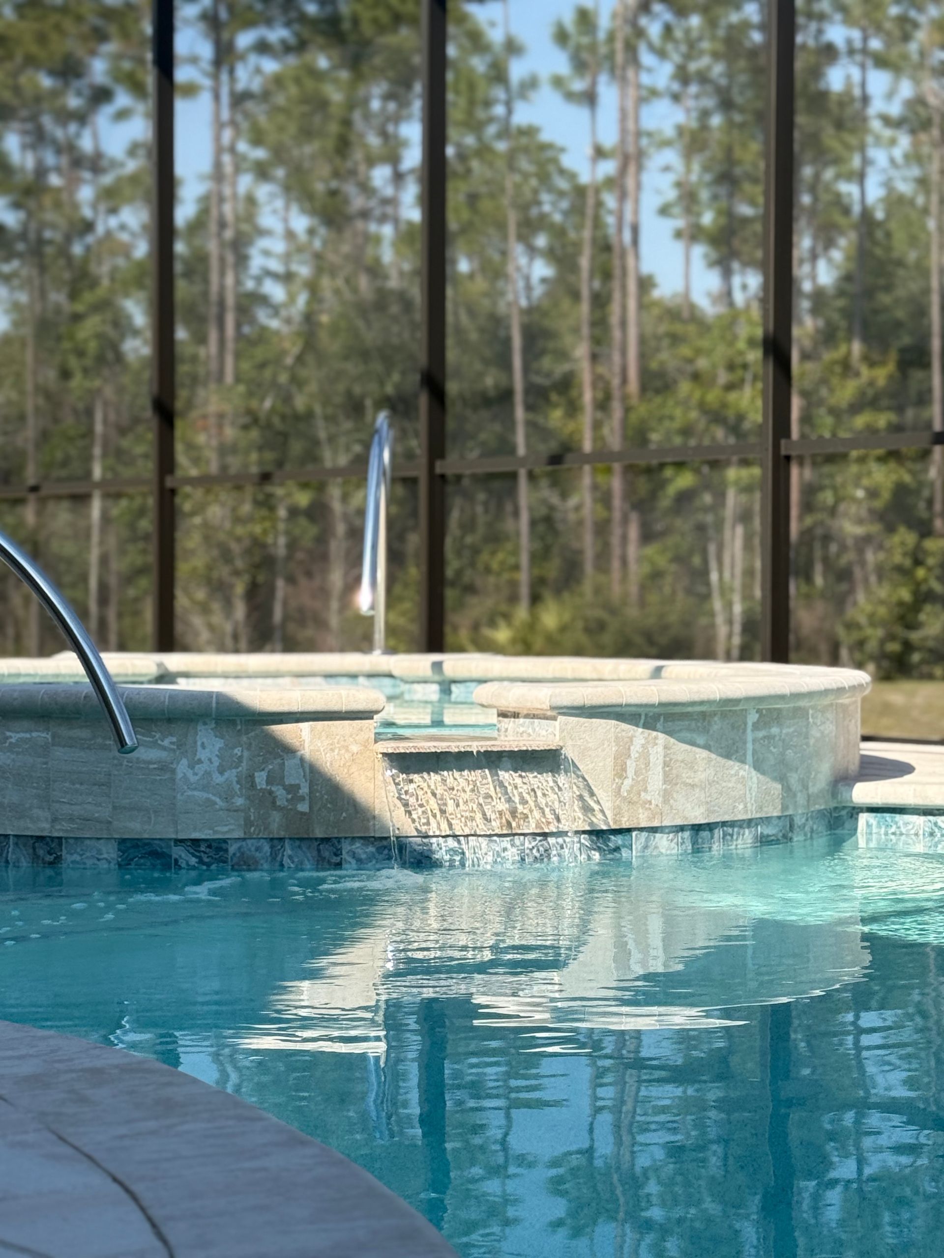Pool with waterfall feature and lush, treed background.