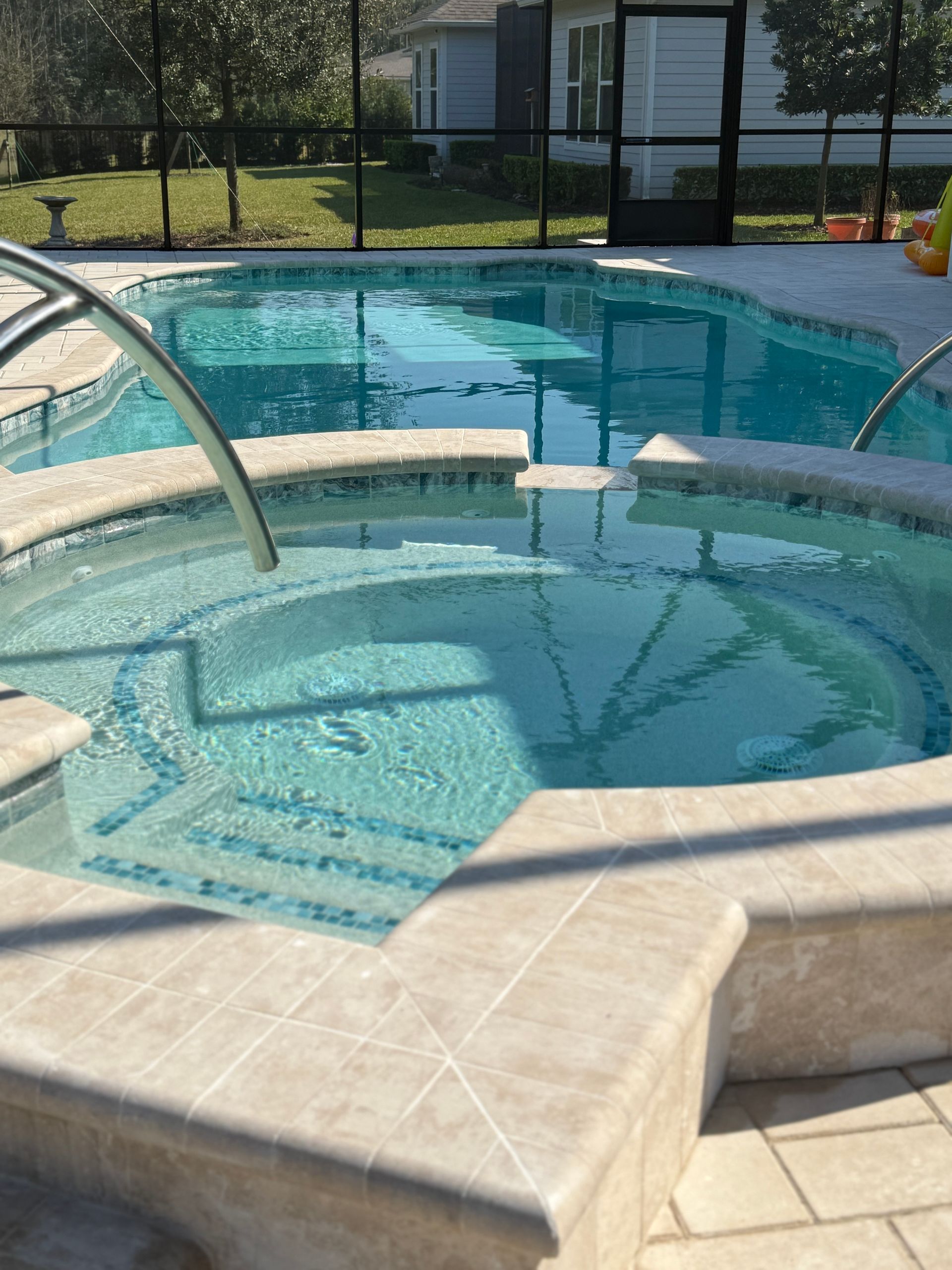 Swimming pool and spa with tan tile surround, blue water, and a screened enclosure.