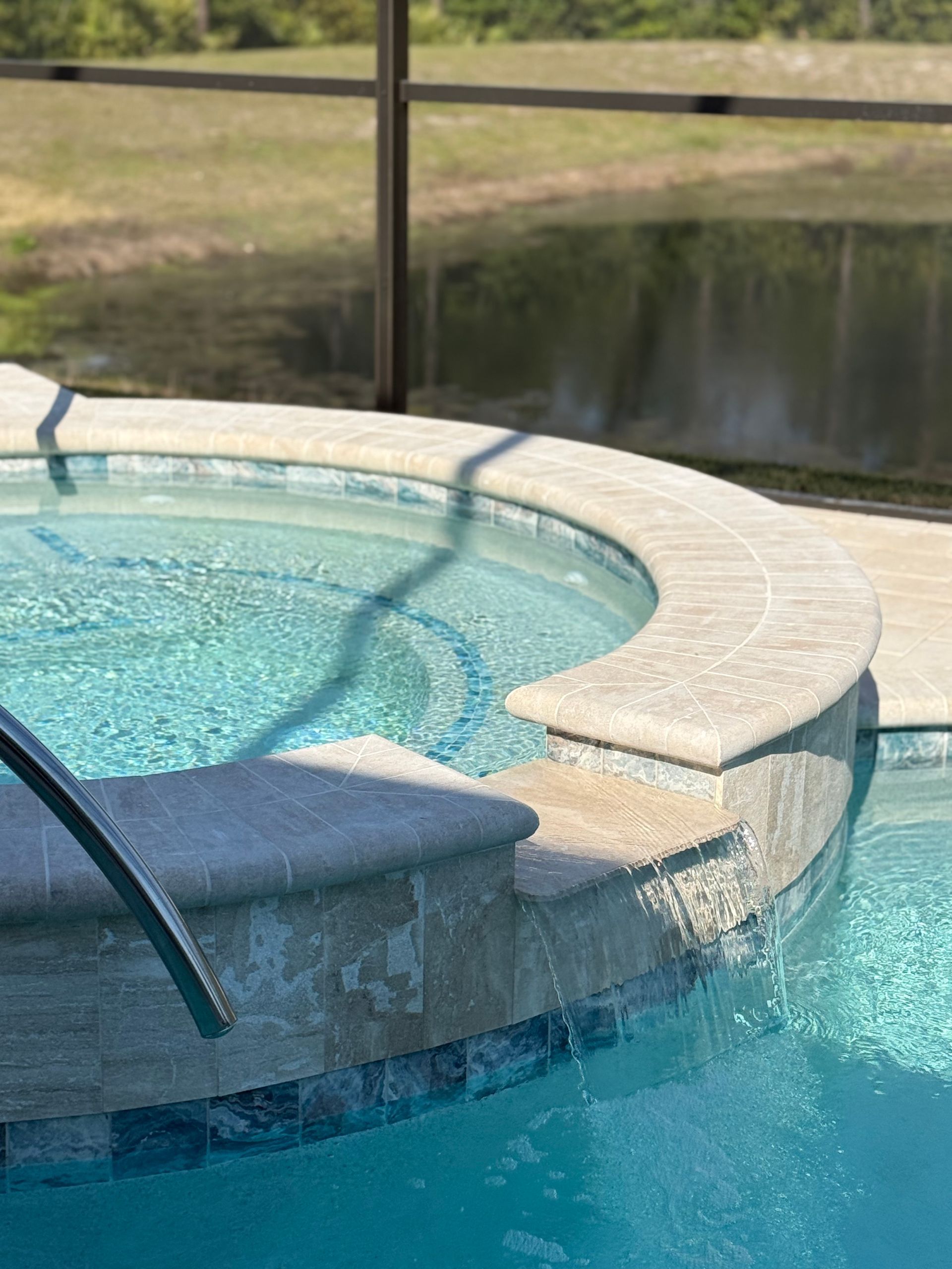 Outdoor hot tub with blue water, tiled edge, and view of grass and sky.