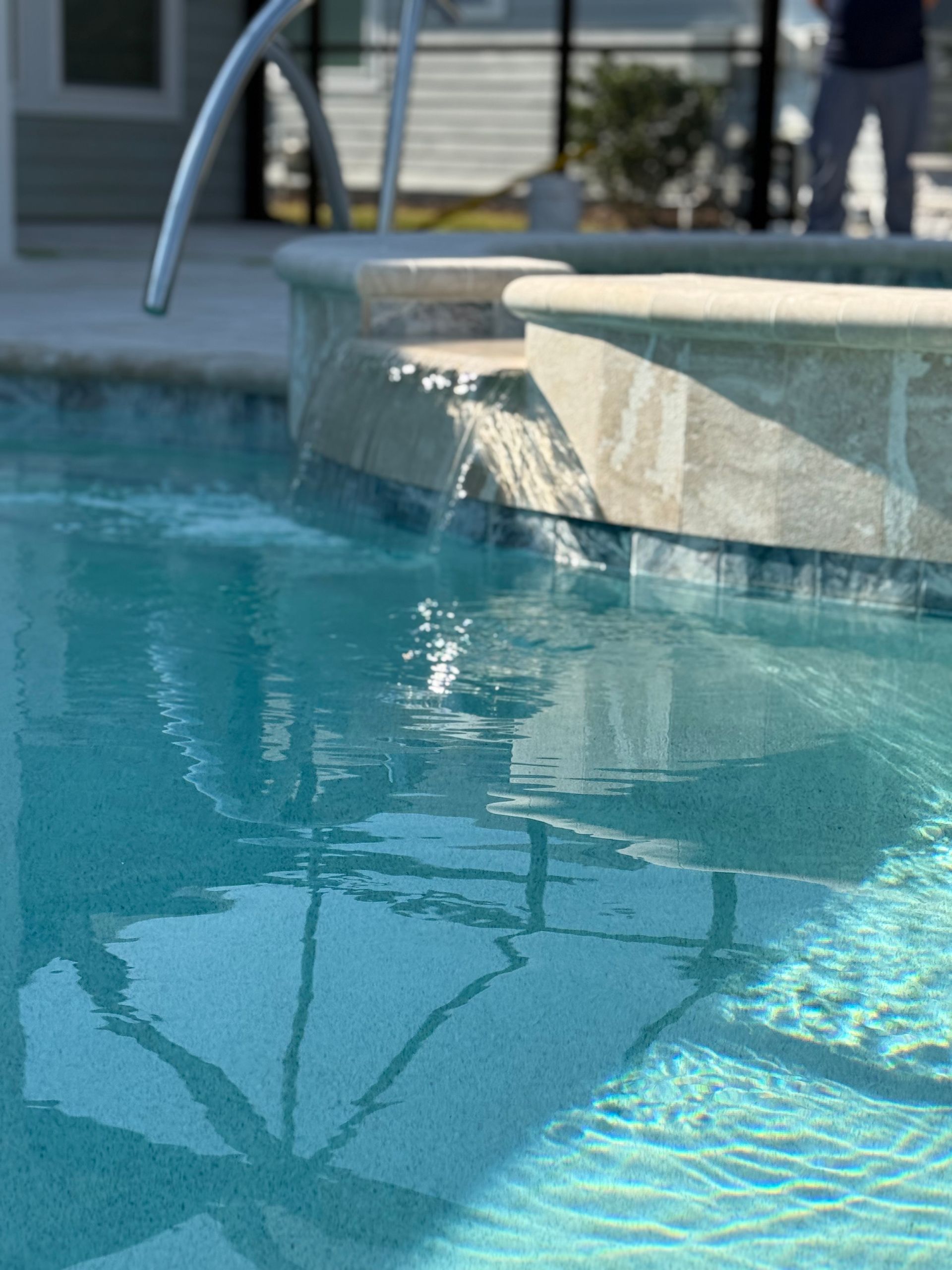 Pool with flowing water feature, turquoise water, sunny outdoor setting.