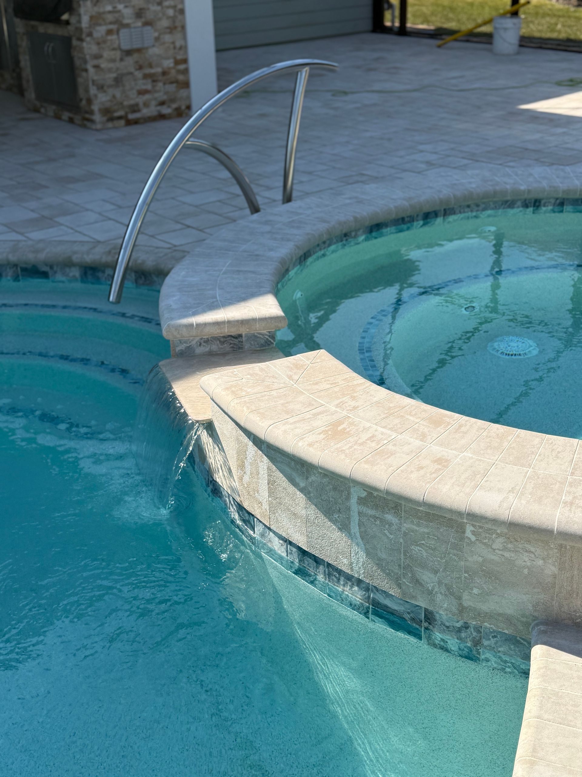 Pool and spa with water cascading over a stone edge, stainless steel handrail.