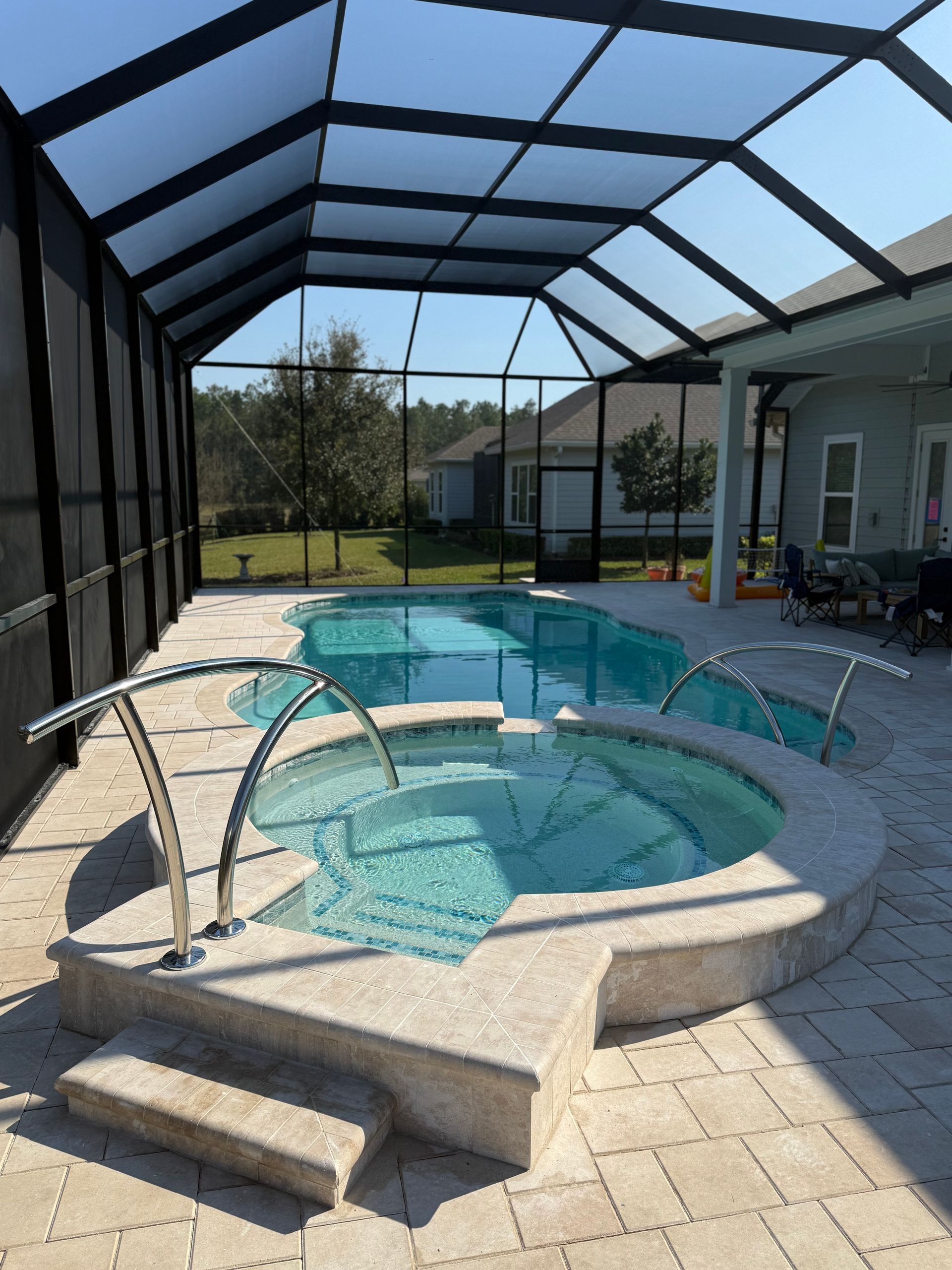 Pool and spa enclosed in a screened lanai; includes stainless steel railings and stone patio.