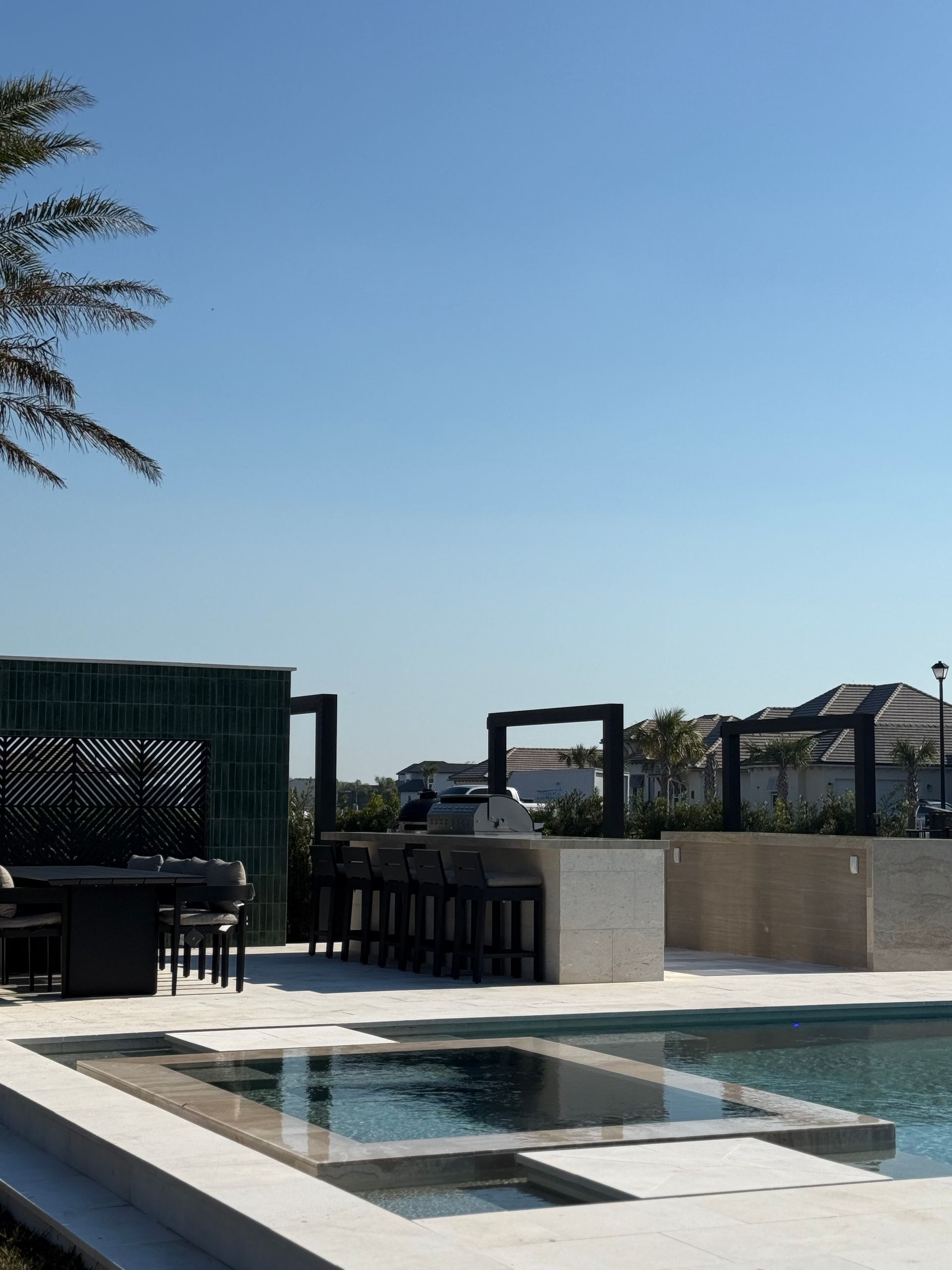 Poolside outdoor kitchen with bar seating, blue sky.