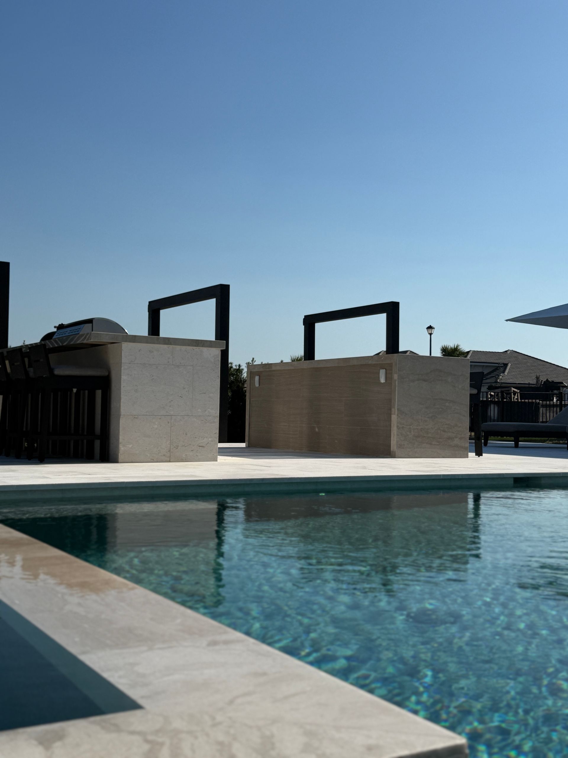 Poolside bar with rectangular arches against a clear blue sky. Sparkling water and light stone accents.