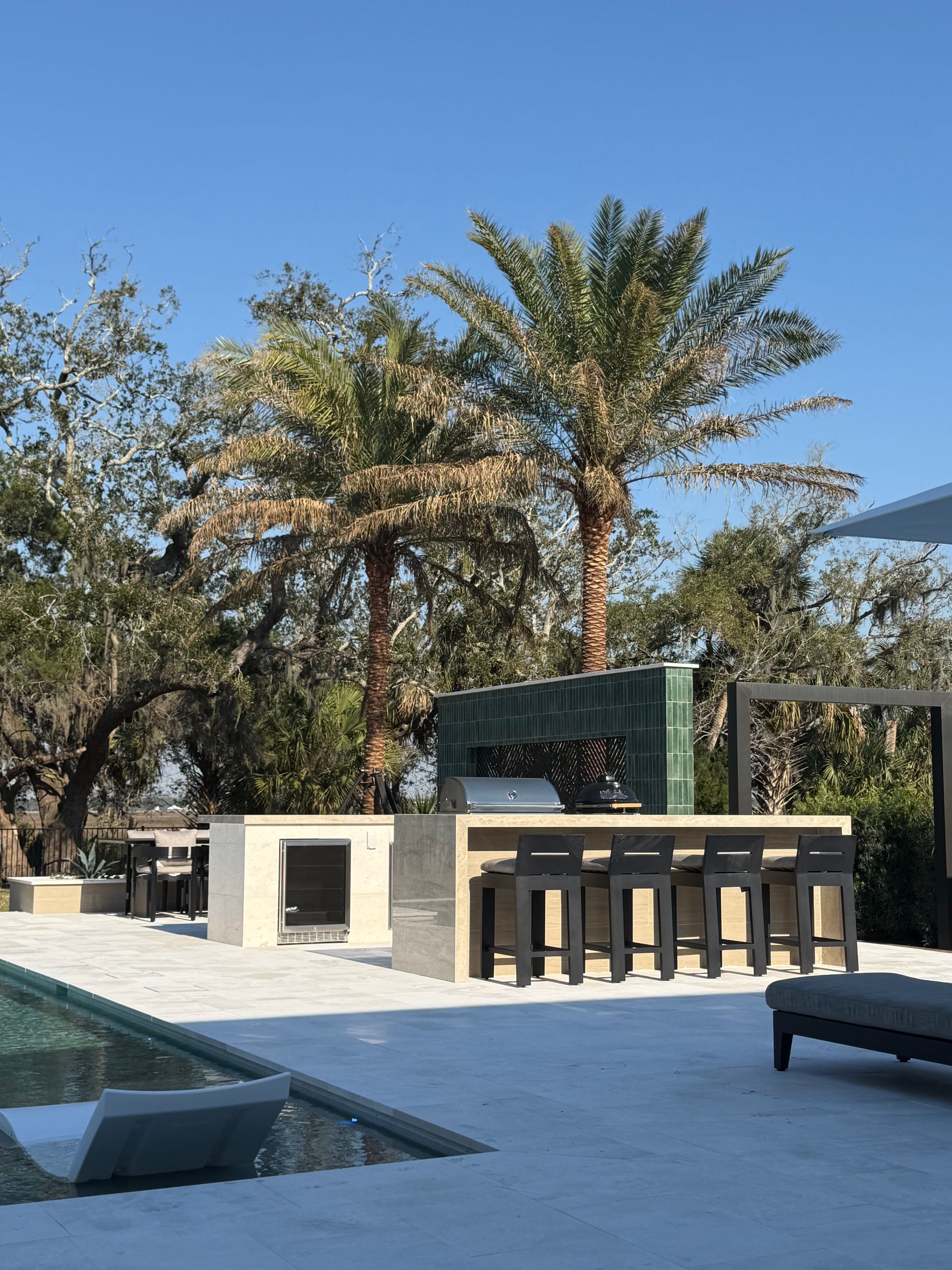 Outdoor kitchen with a bar and palm trees under a clear blue sky.