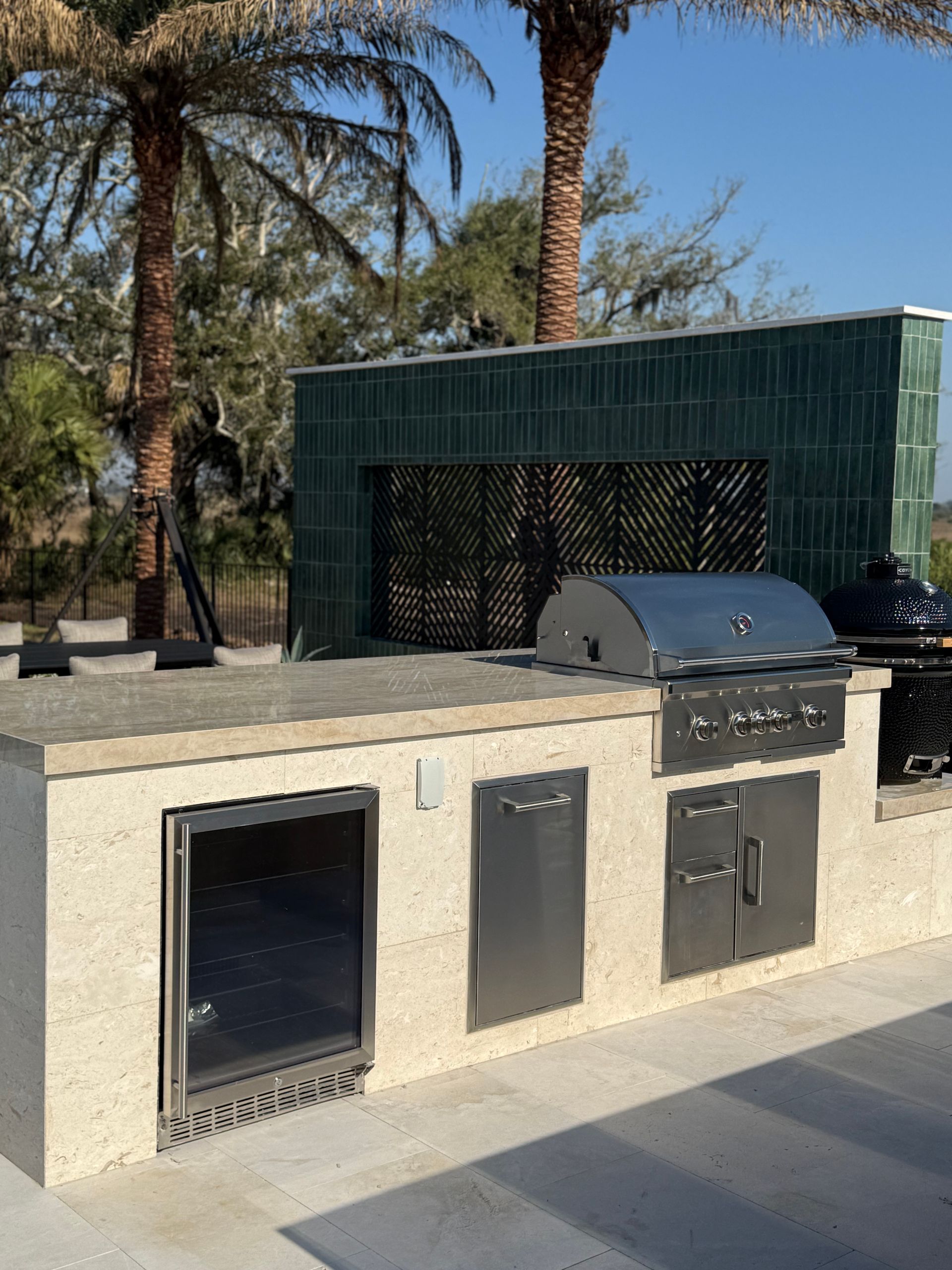 Outdoor kitchen with stainless steel appliances and green tiled backsplash.