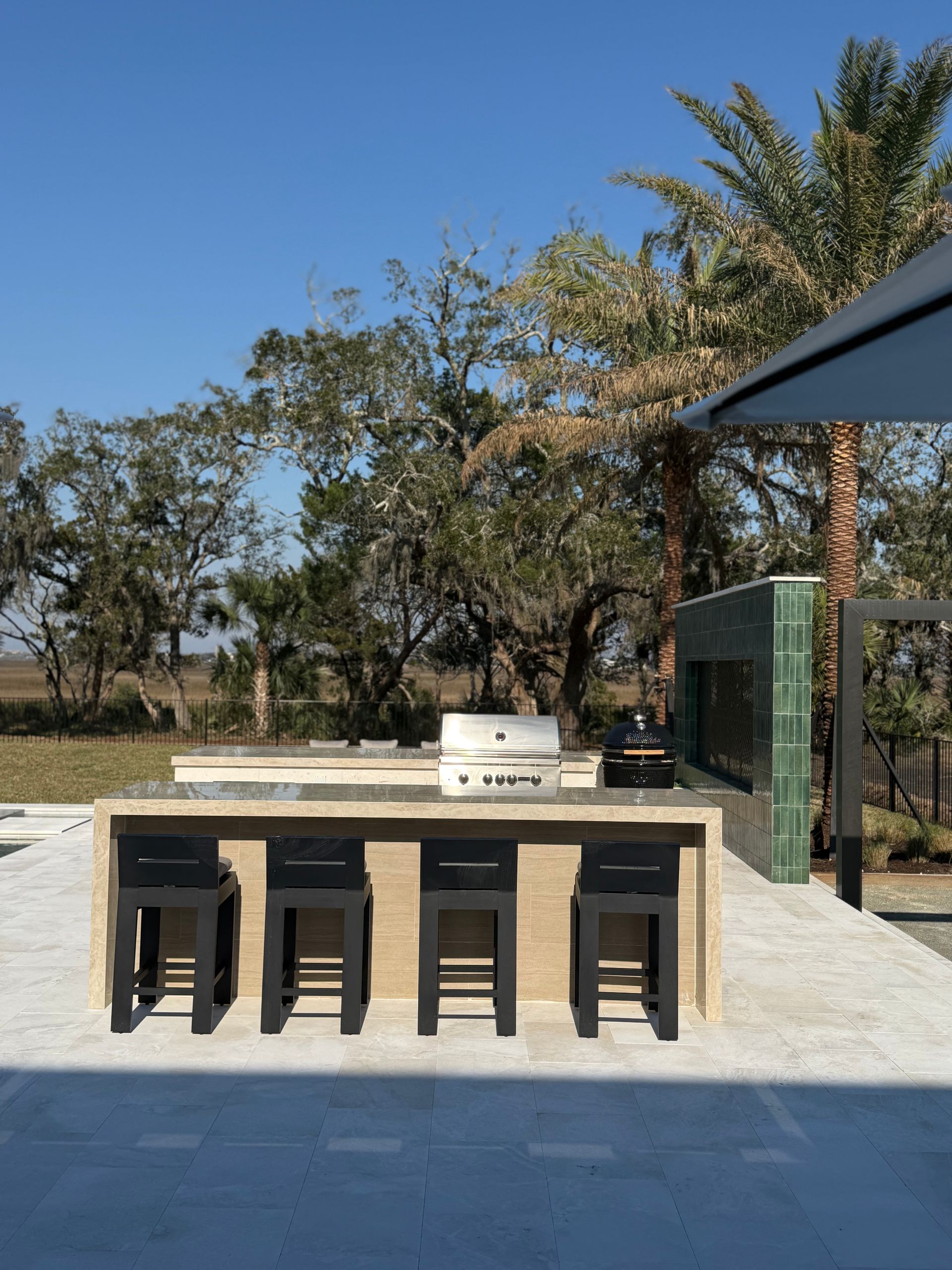 Outdoor kitchen with grill, bar, and stools on a sunny day.