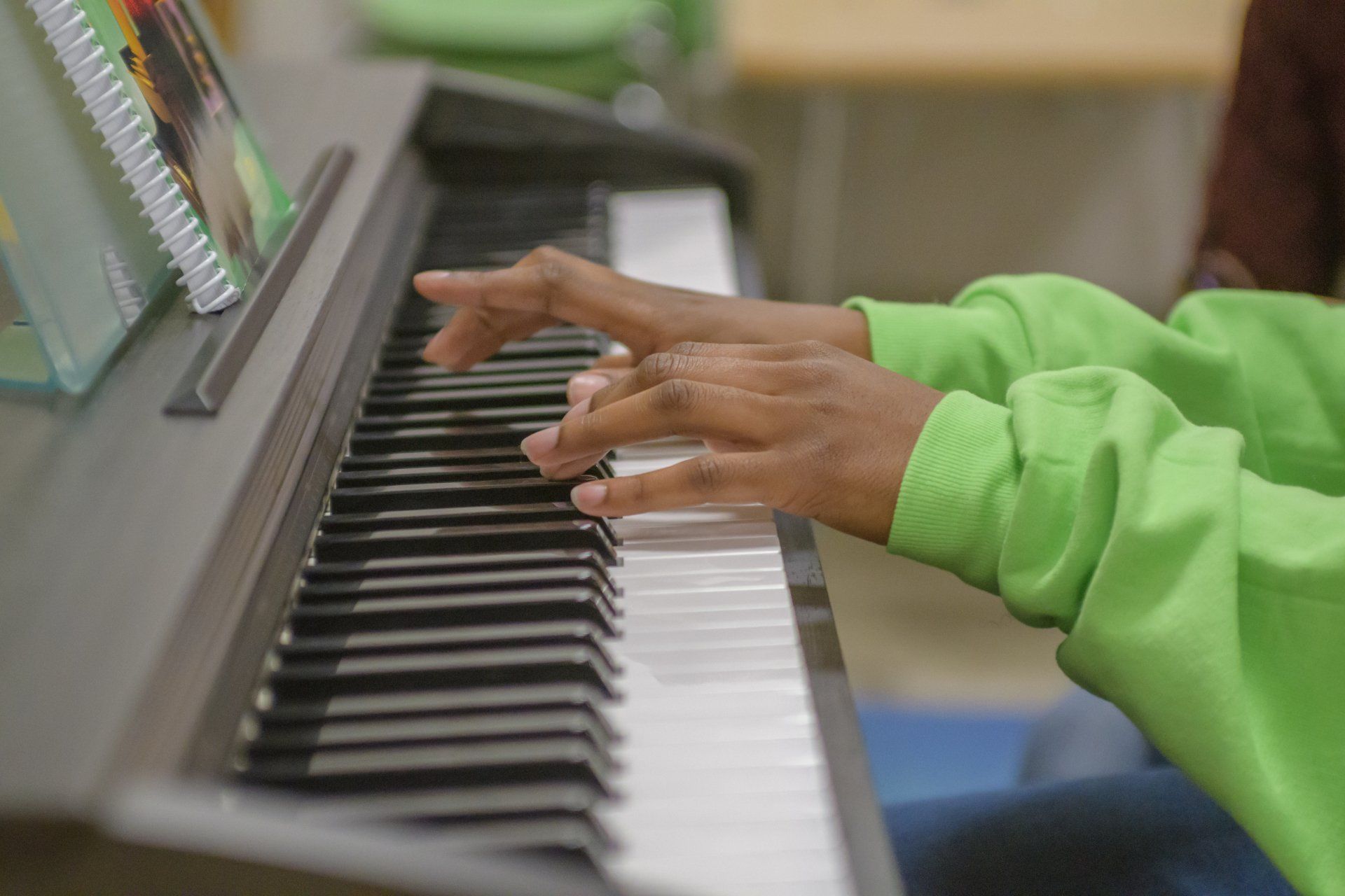 A person in a green sweater is playing a piano in a classroom.