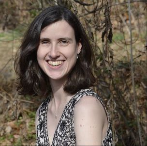 A woman in a black and white dress is smiling in front of a tree.