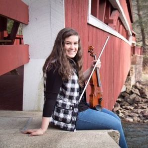 A woman is sitting on a bridge holding a violin.