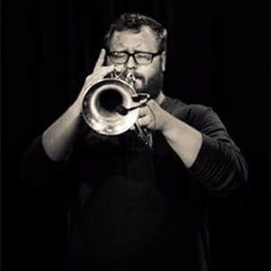 A man with glasses is playing a trumpet in a black and white photo.