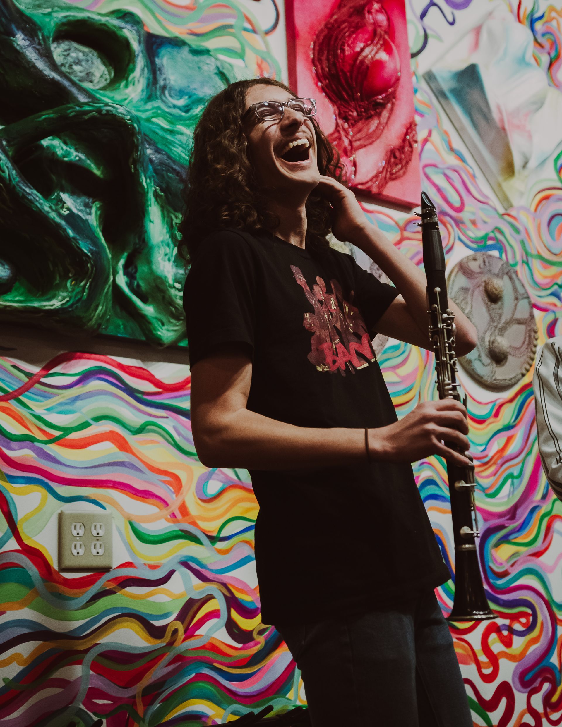 A man is playing a clarinet in front of a colorful wall.