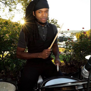 A man with dreadlocks is playing drums outside