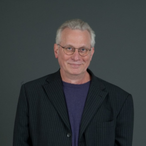 A man in a suit and glasses is smiling for the camera