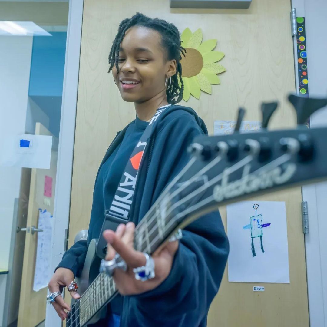 A woman playing a guitar with a strap that says i love nyc